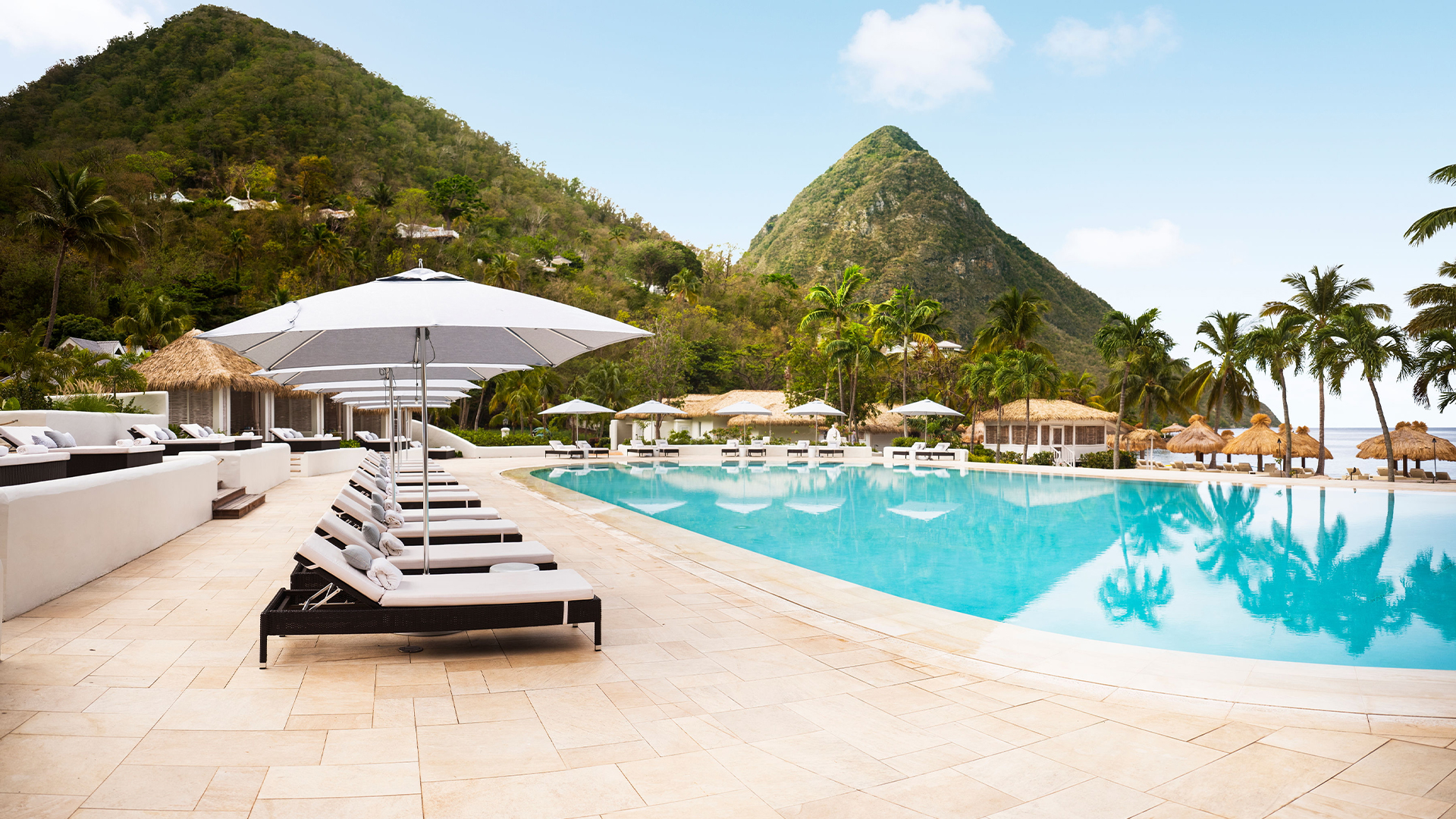 A luxury resort poolside with loungers and umbrellas, overlooking a lush mountain.