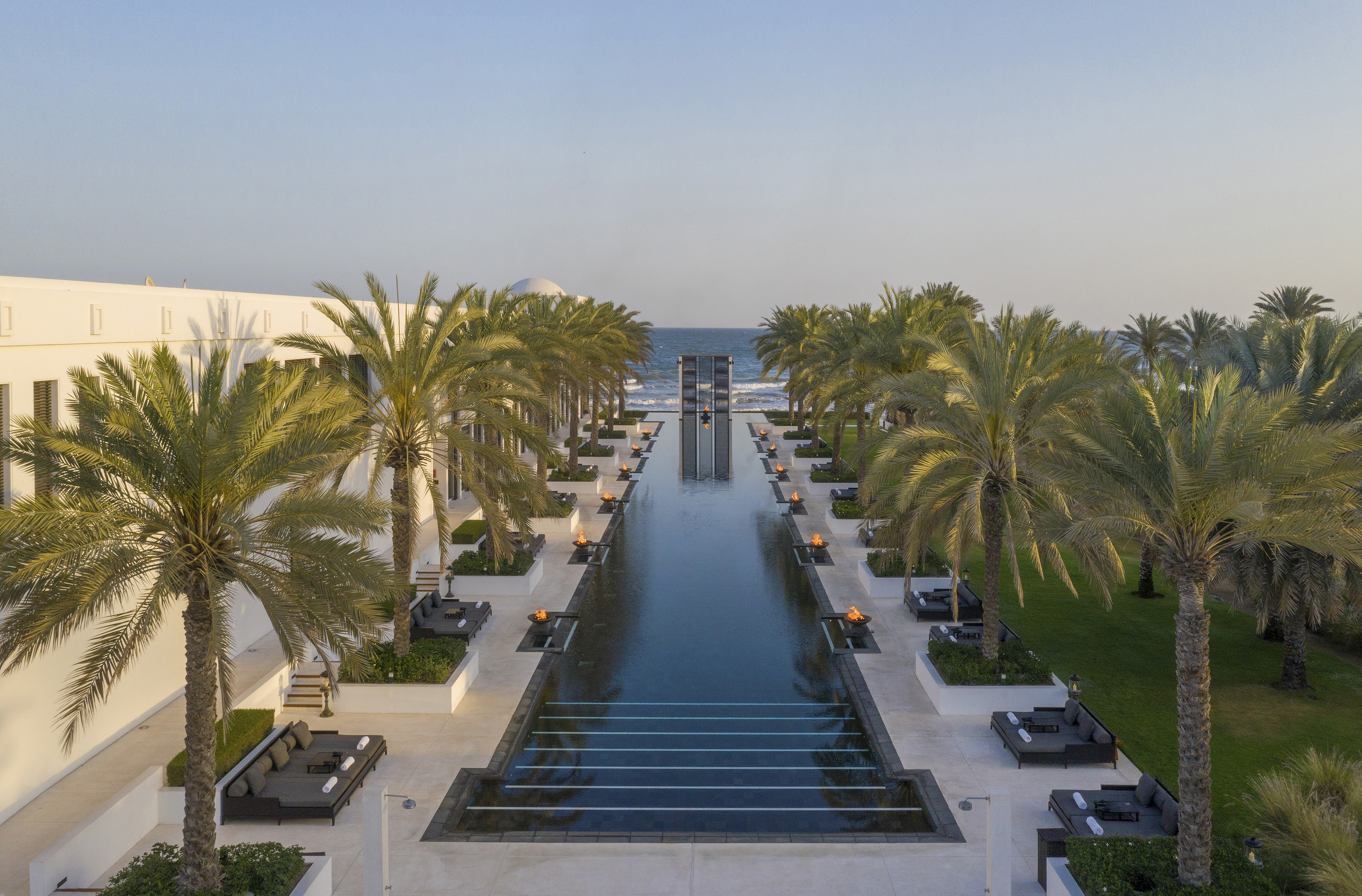 The long swimming pool at The Chedi Muscat stretching towards the sea flanked by palm trees