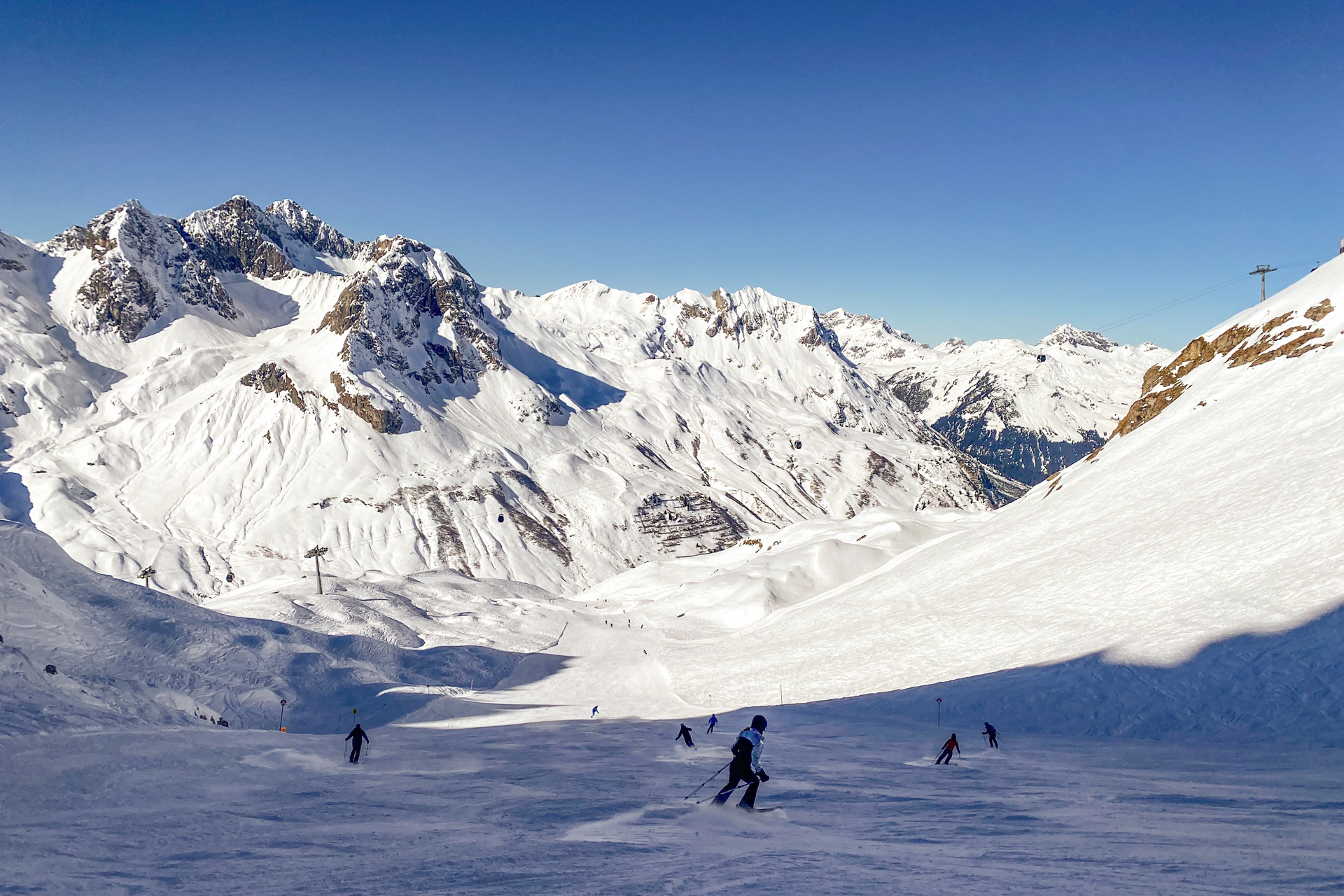 A group of skiers going downhill with snowy rocky mountains in the background