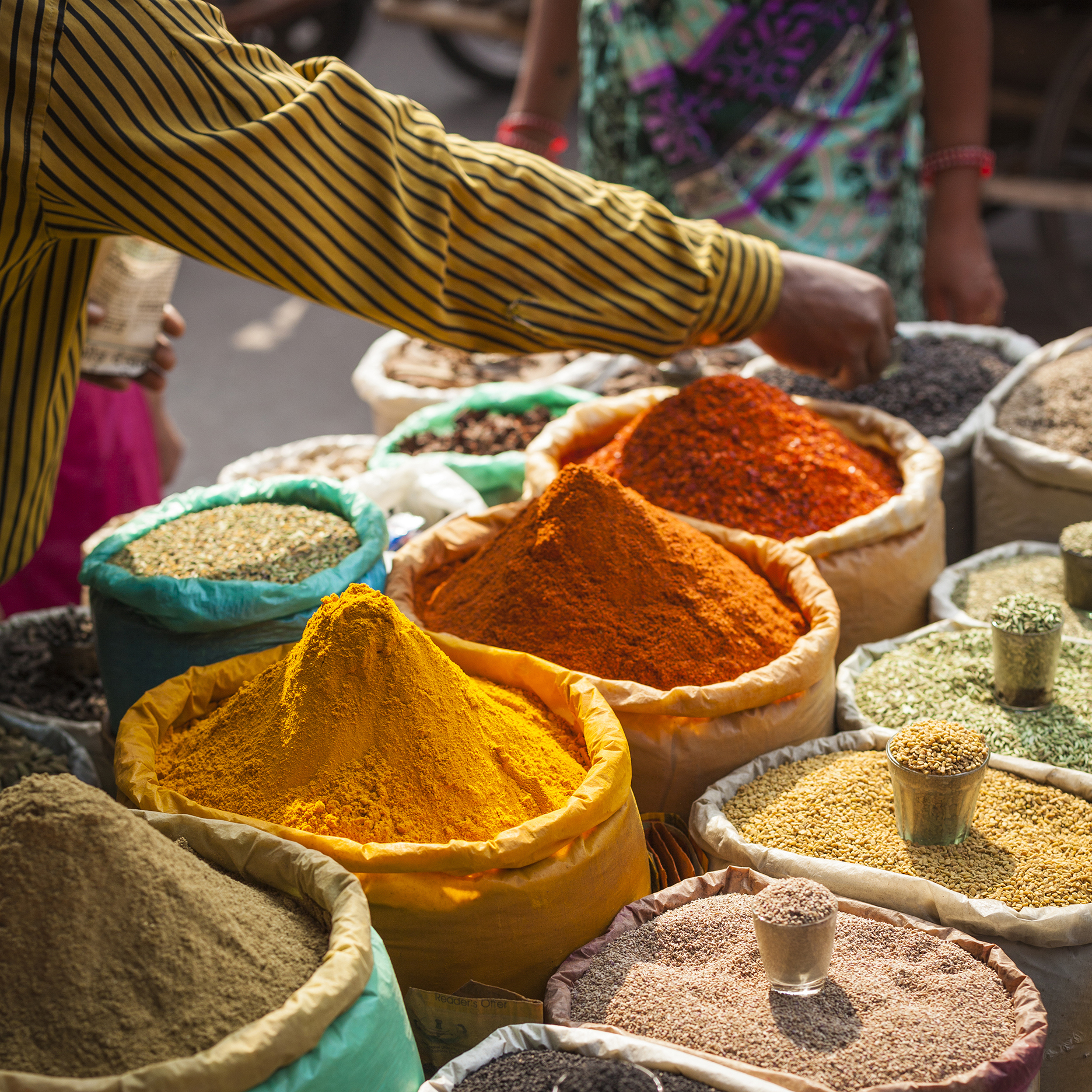 Man in striped shirt picking colourful spices from bags at a market