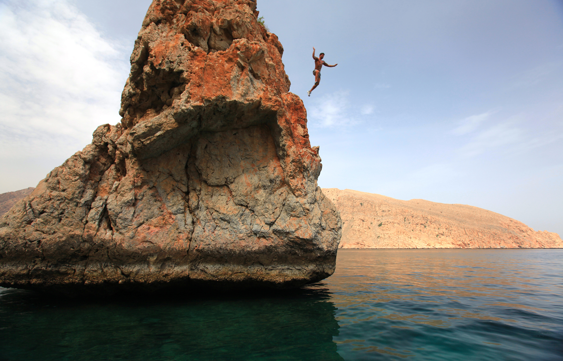 A man jumping from a tall rocky point into the sea