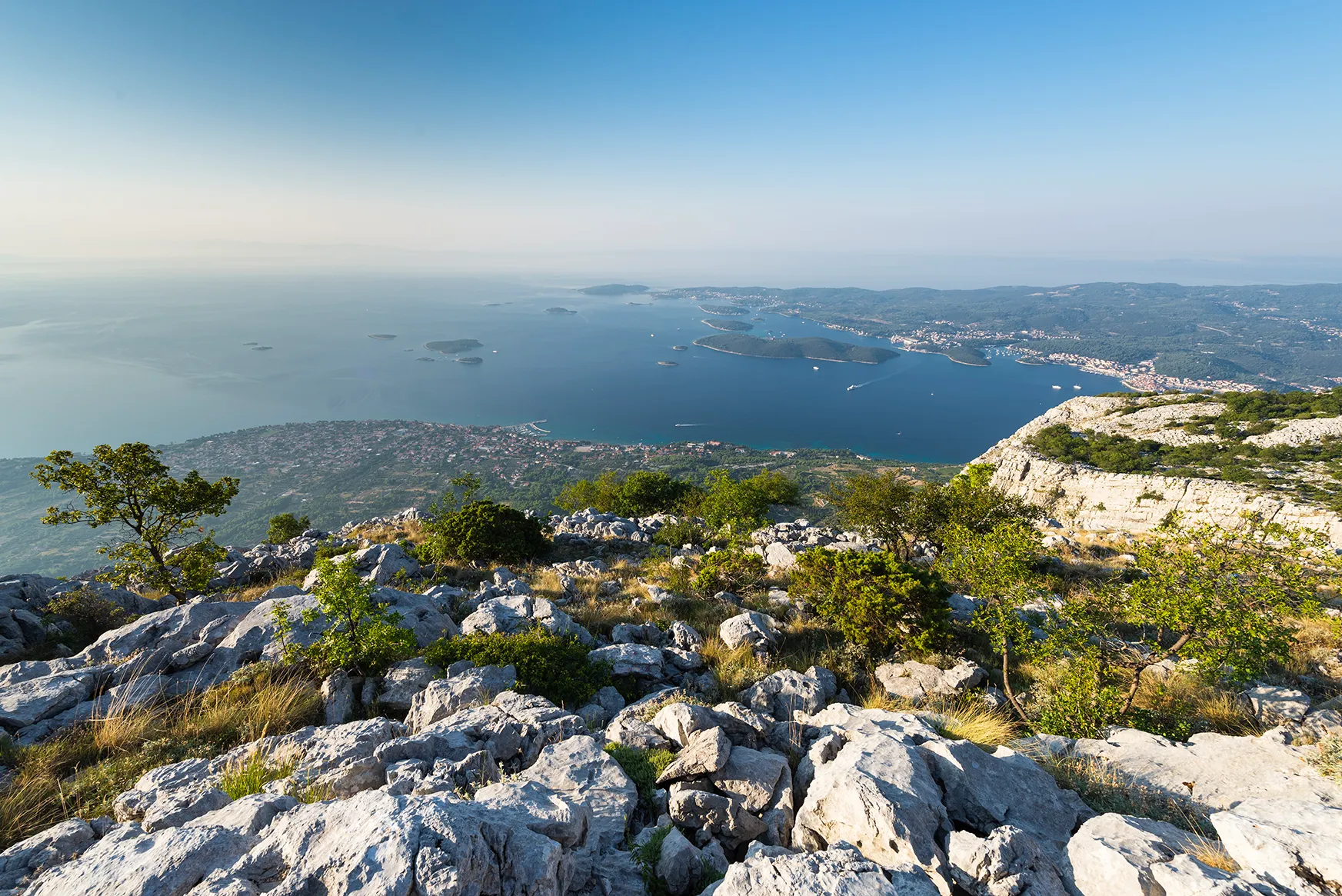 Rocky mountaintop overlooking a blue Adriatic coastline dotted with islands and bays.