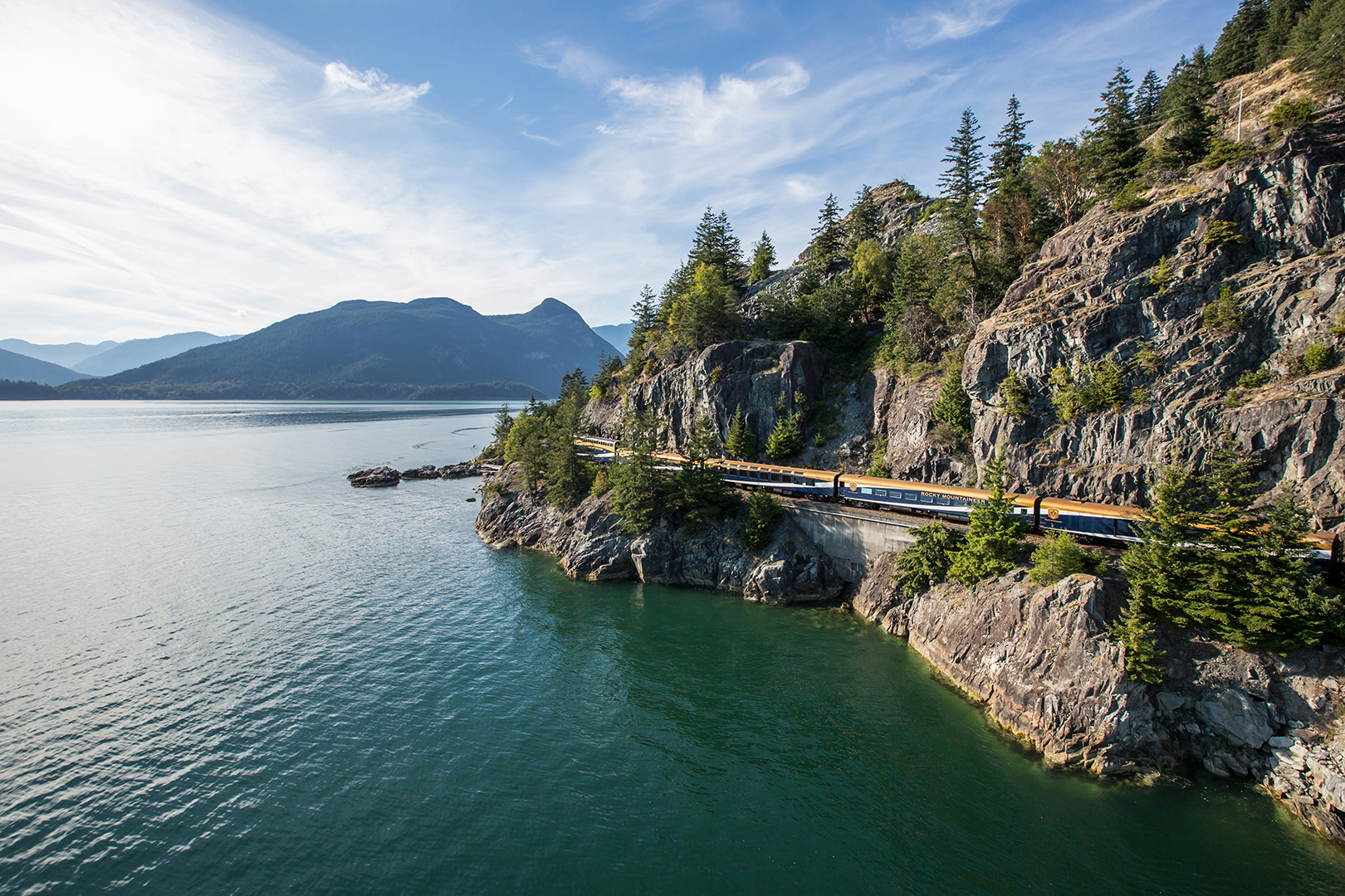 Rocky Mountaineer train crossing tracks by a bay in Canada