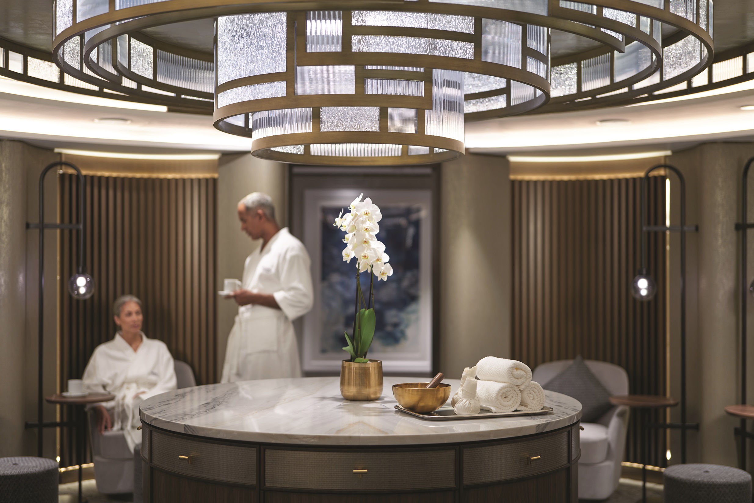 Luxurious Oceania Cruises Aquamar spa lounge with orchid centerpiece, rolled towels, and guests in white robes.