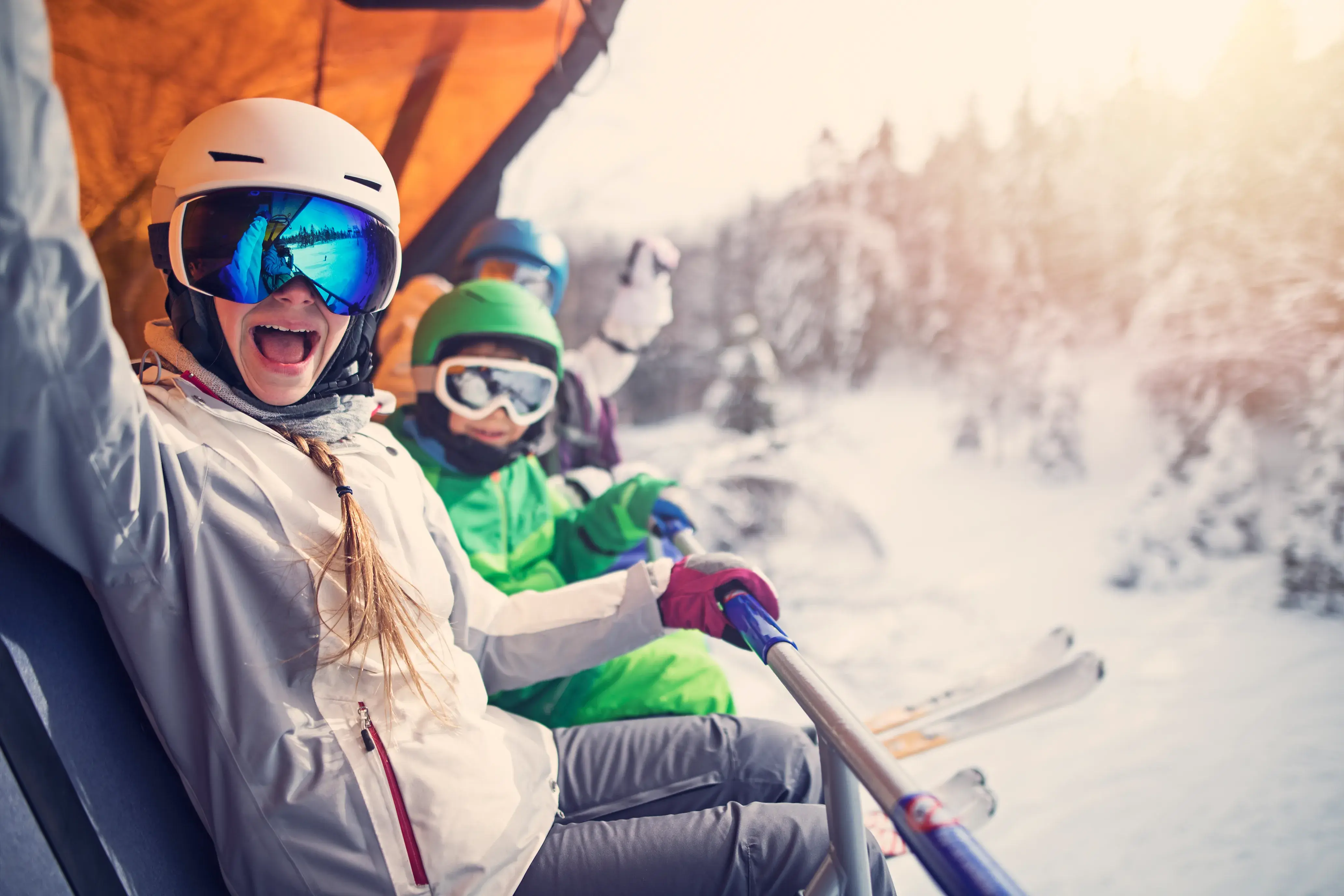 Group of skiers wearing colourful winter gear riding a ski lift over a snowy mountain landscape.