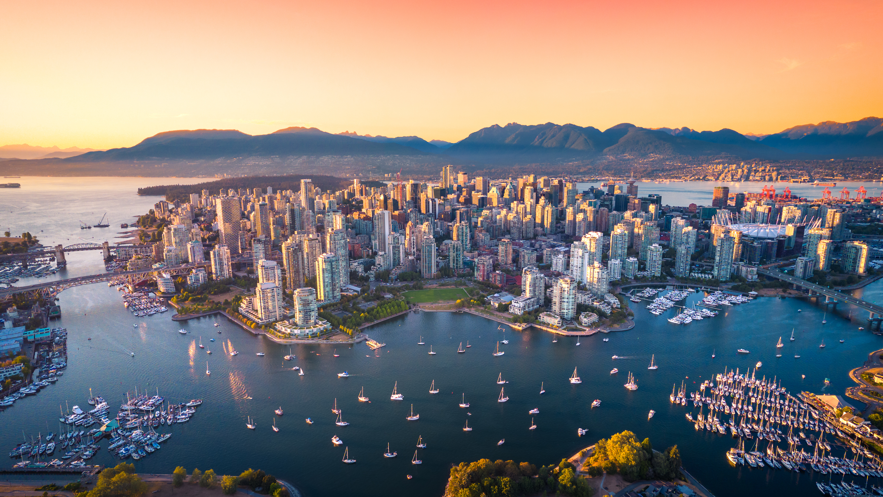 Aerial view of a densely populated city with skyscrapers near a waterfront at sunset.
