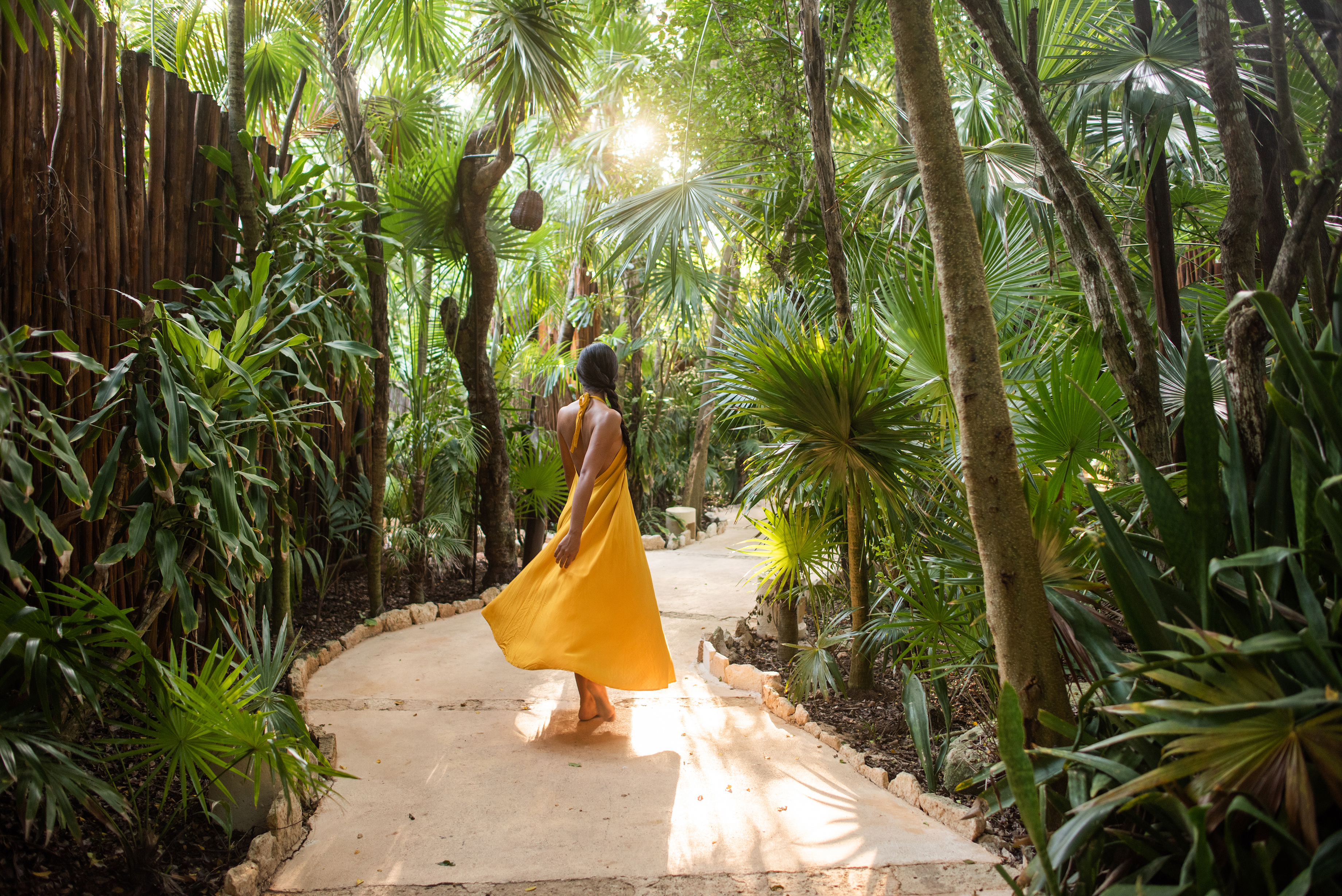 A woman in a yellow dress walking along a lush green pathway at Viceroy Riviera Maya