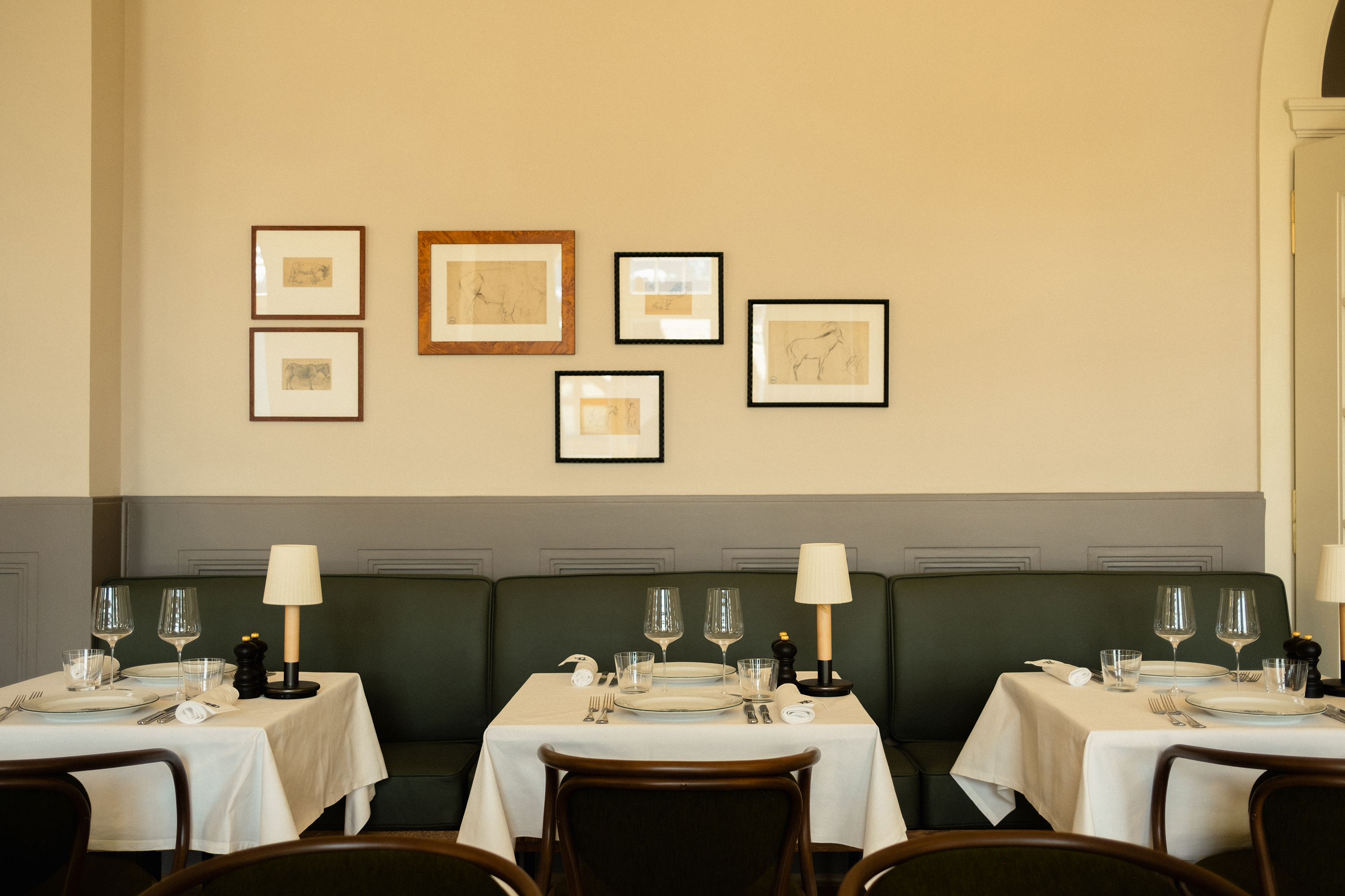 Three dining tables set for dinner in front of a wall featuring framed pictures