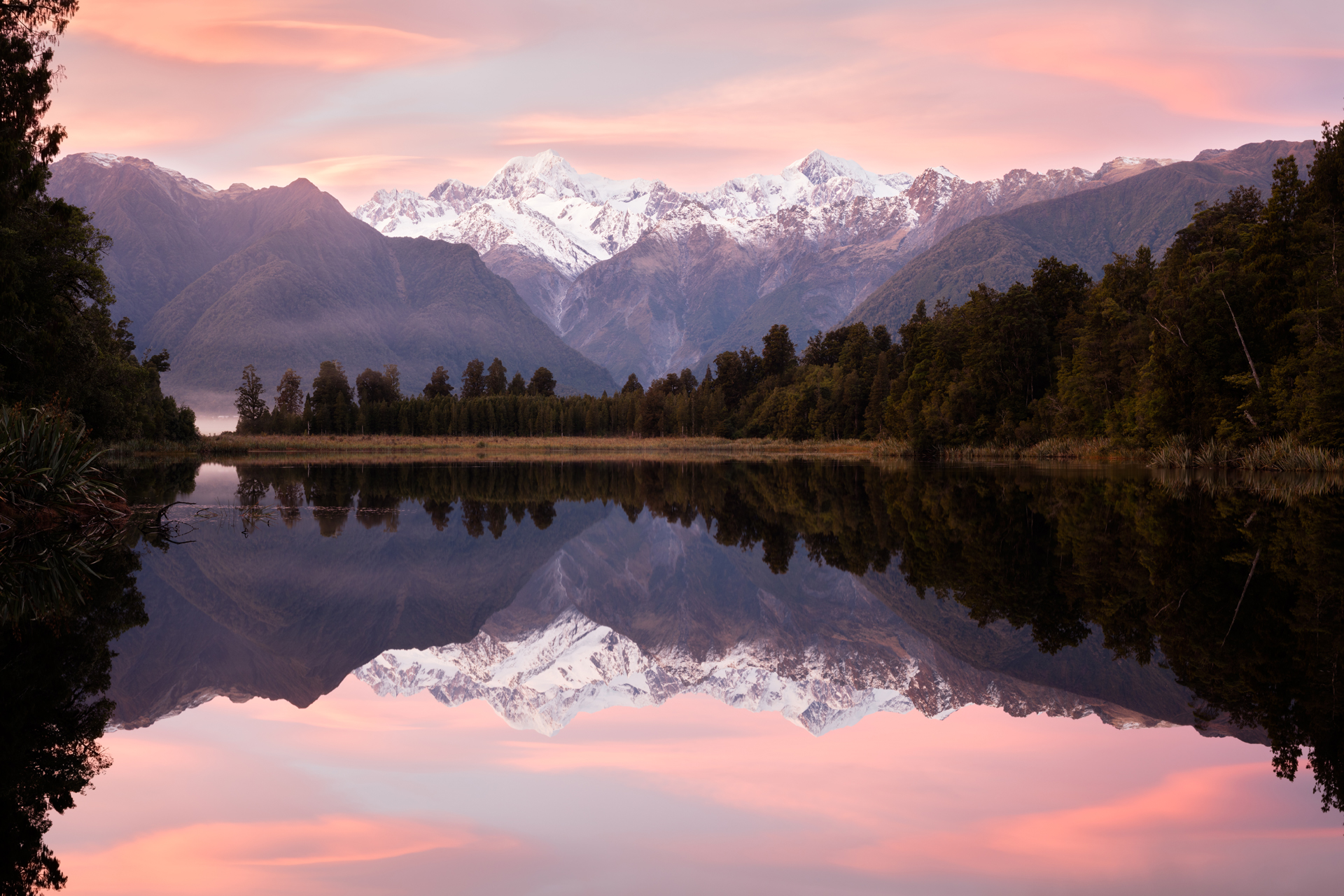A view across Lake Matheson, New Zealand with snow capped mountains in the back