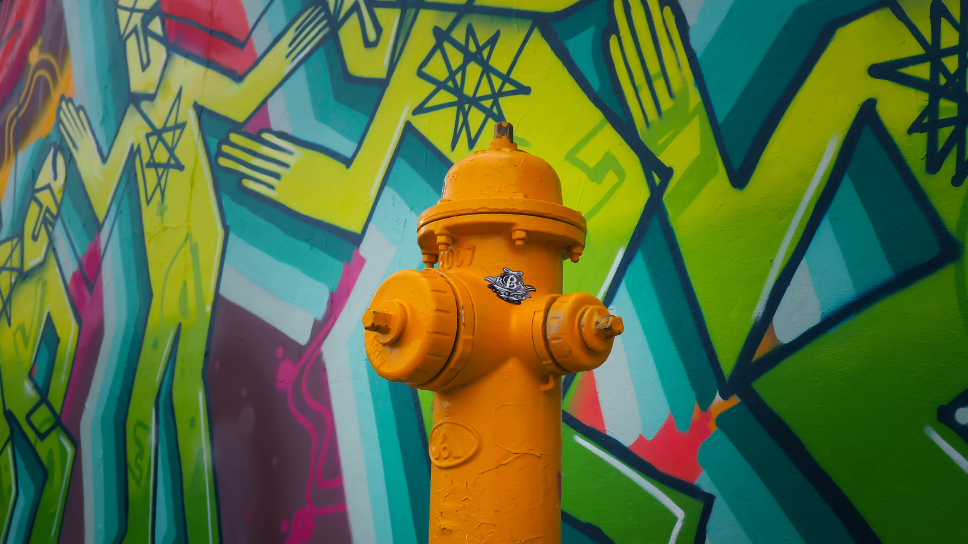 An orange fire hydrant on front of street art on a wall