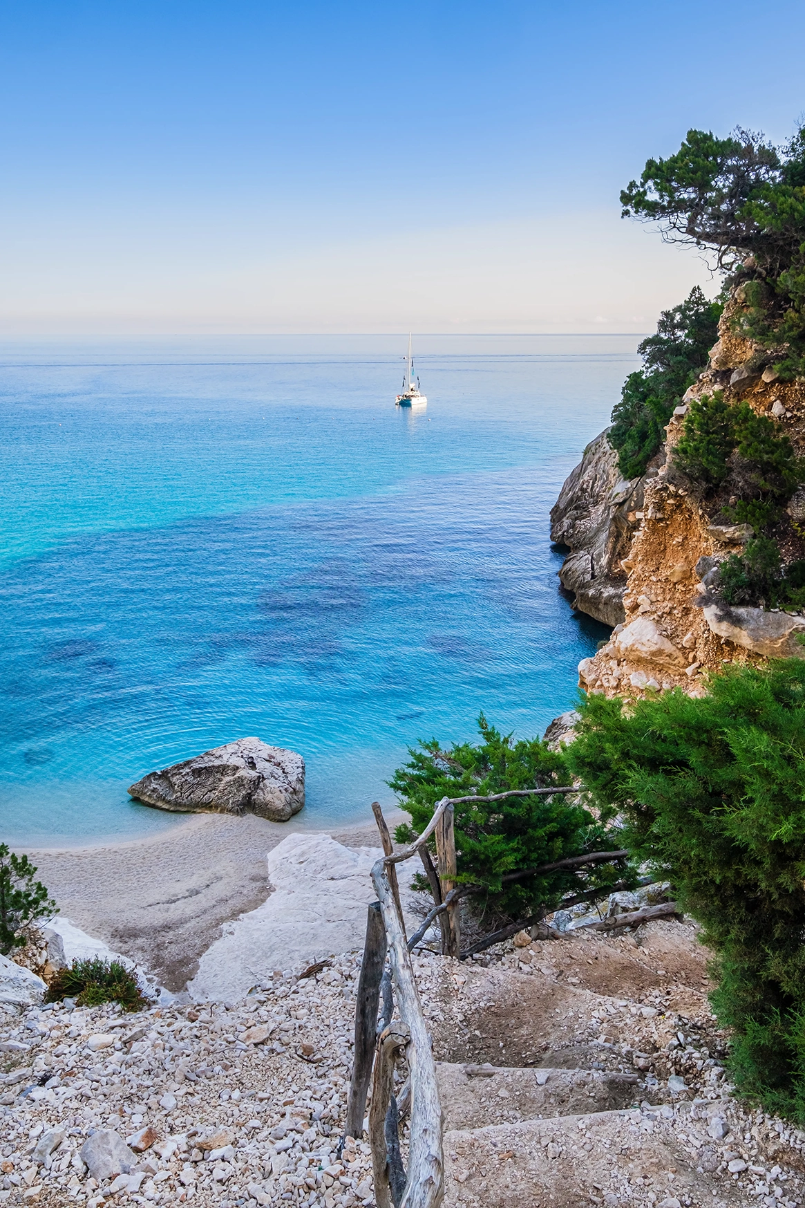 Looking out to a boat at sea from the steps of a rocky coastline in Sardinia