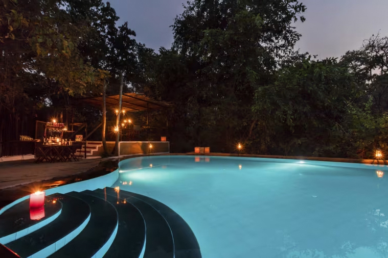 Pool and bar lit up at night at Reni Pani Jungle Lodge