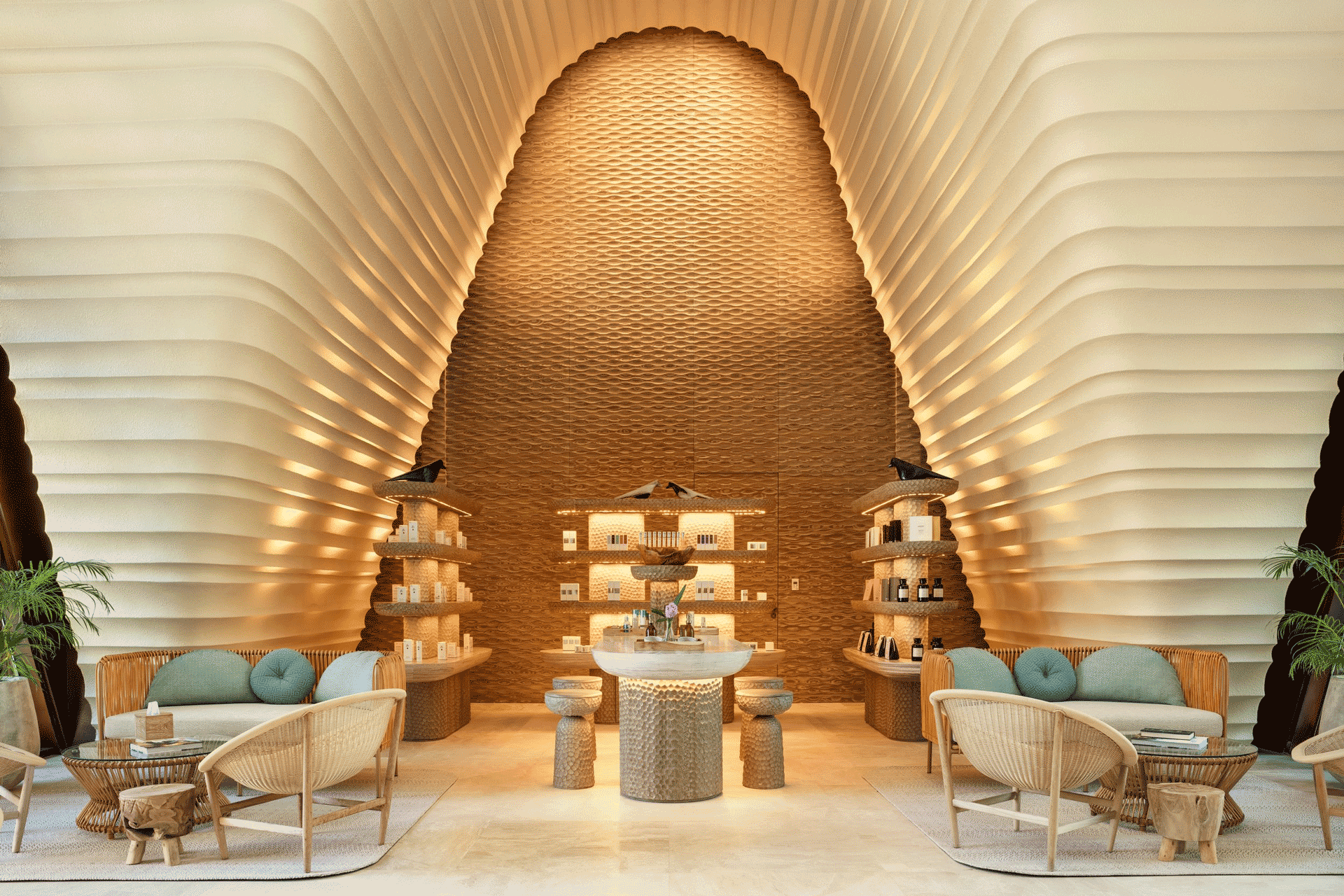 Modern spa interior with curved textured walls, soft lighting, and seating around a central display of wellness products.