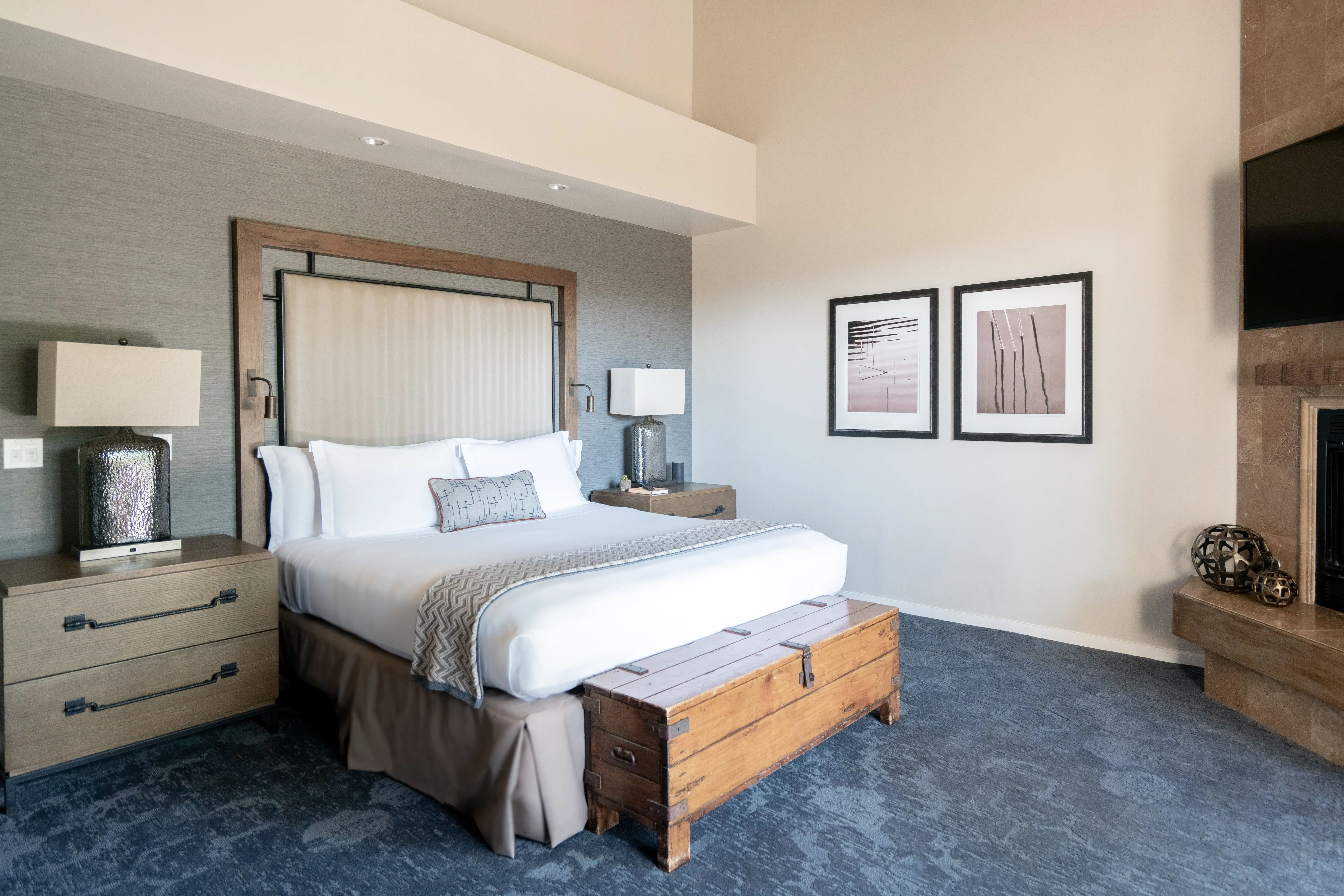 The bedroom of a Ranch Suite at Carmel Valley Ranch in California featuring a large bed with white linens, rustic furniture and modern design with a glimpse of a fireplace