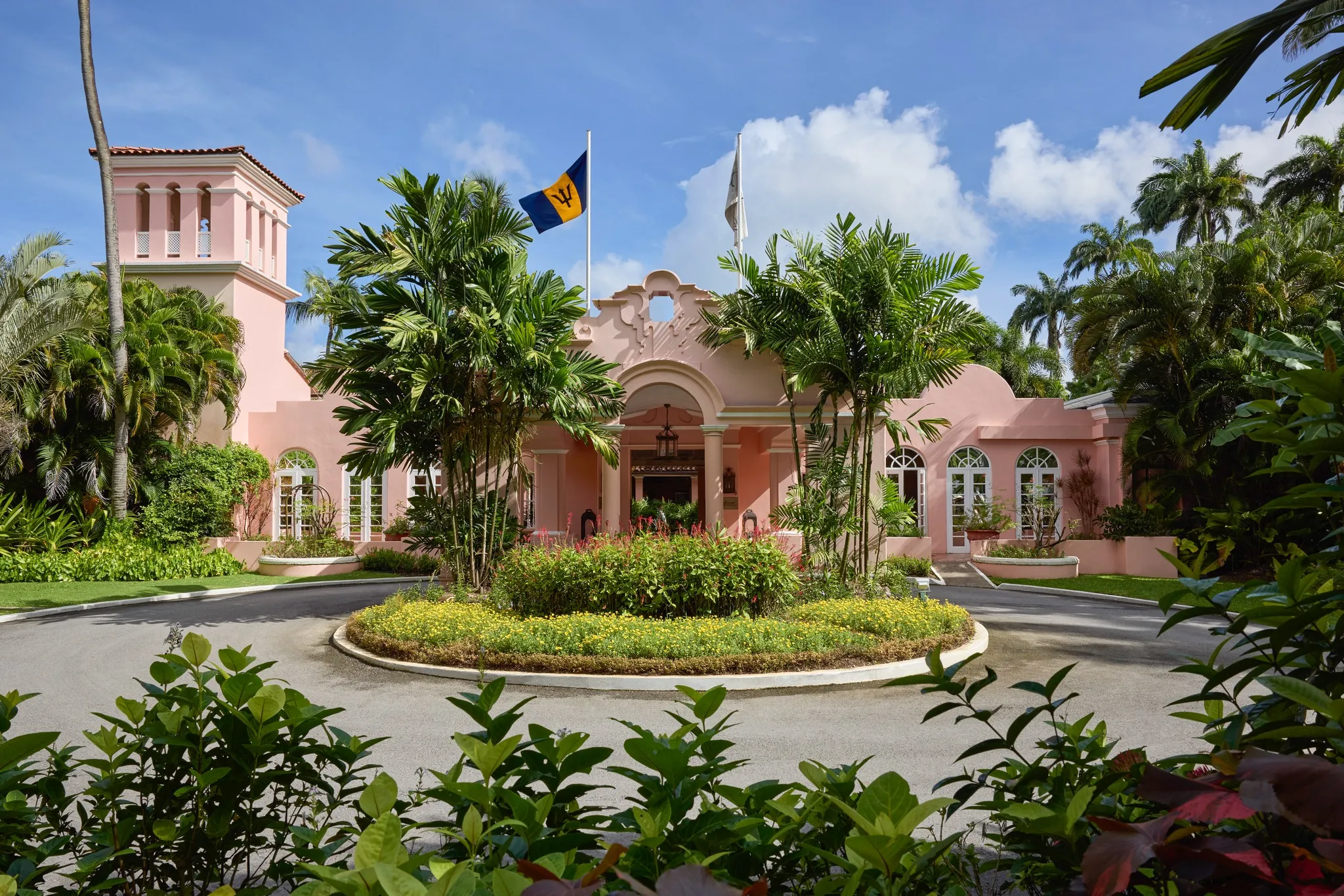 The pink exterior of Fairmont Royal Pavilion in Barbados surrounded by tropical gardens and flying a flag