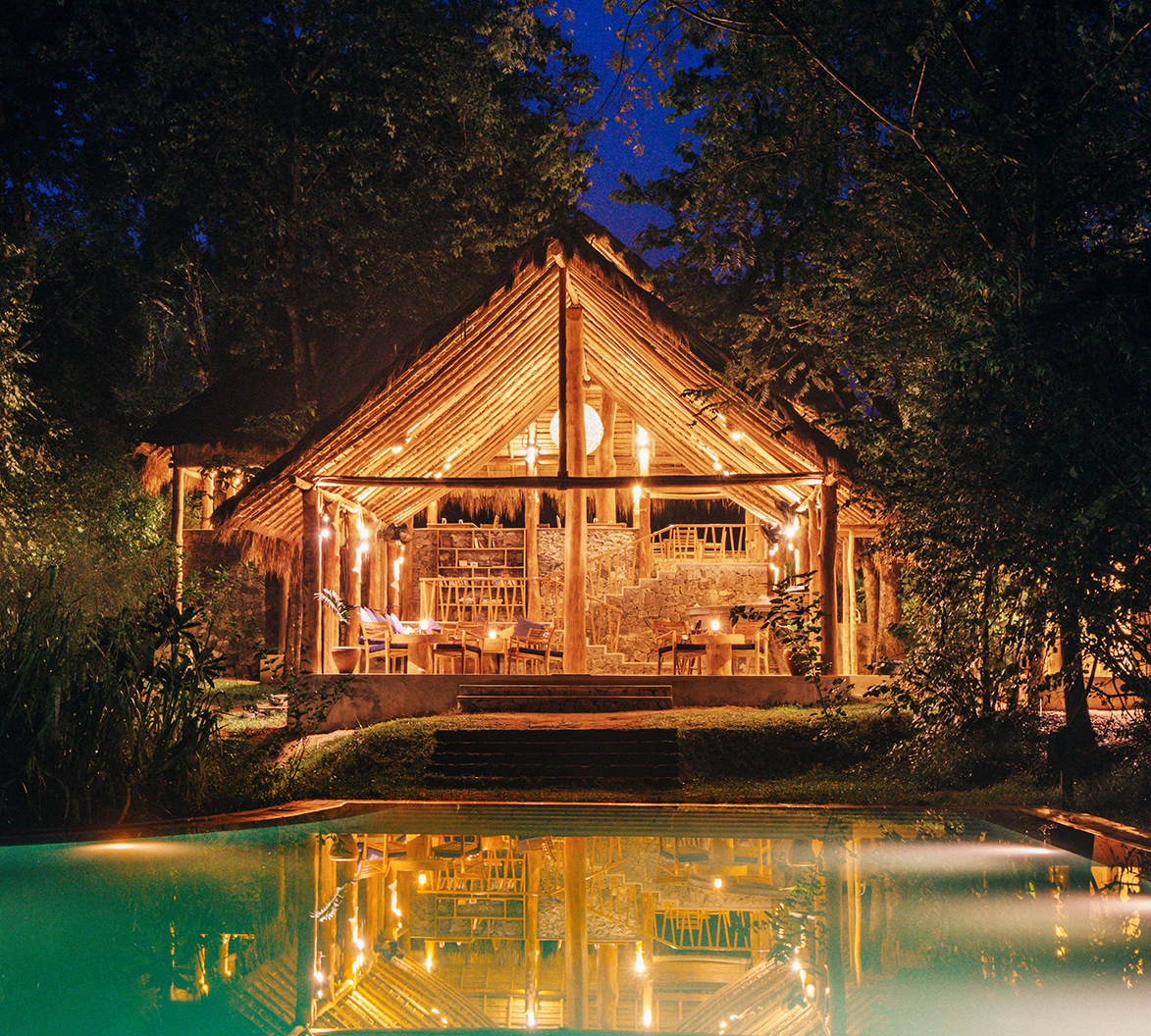 Asia, Sri Lanka, Gal Oya Lodge, view of commual hut from pool at night, lit up