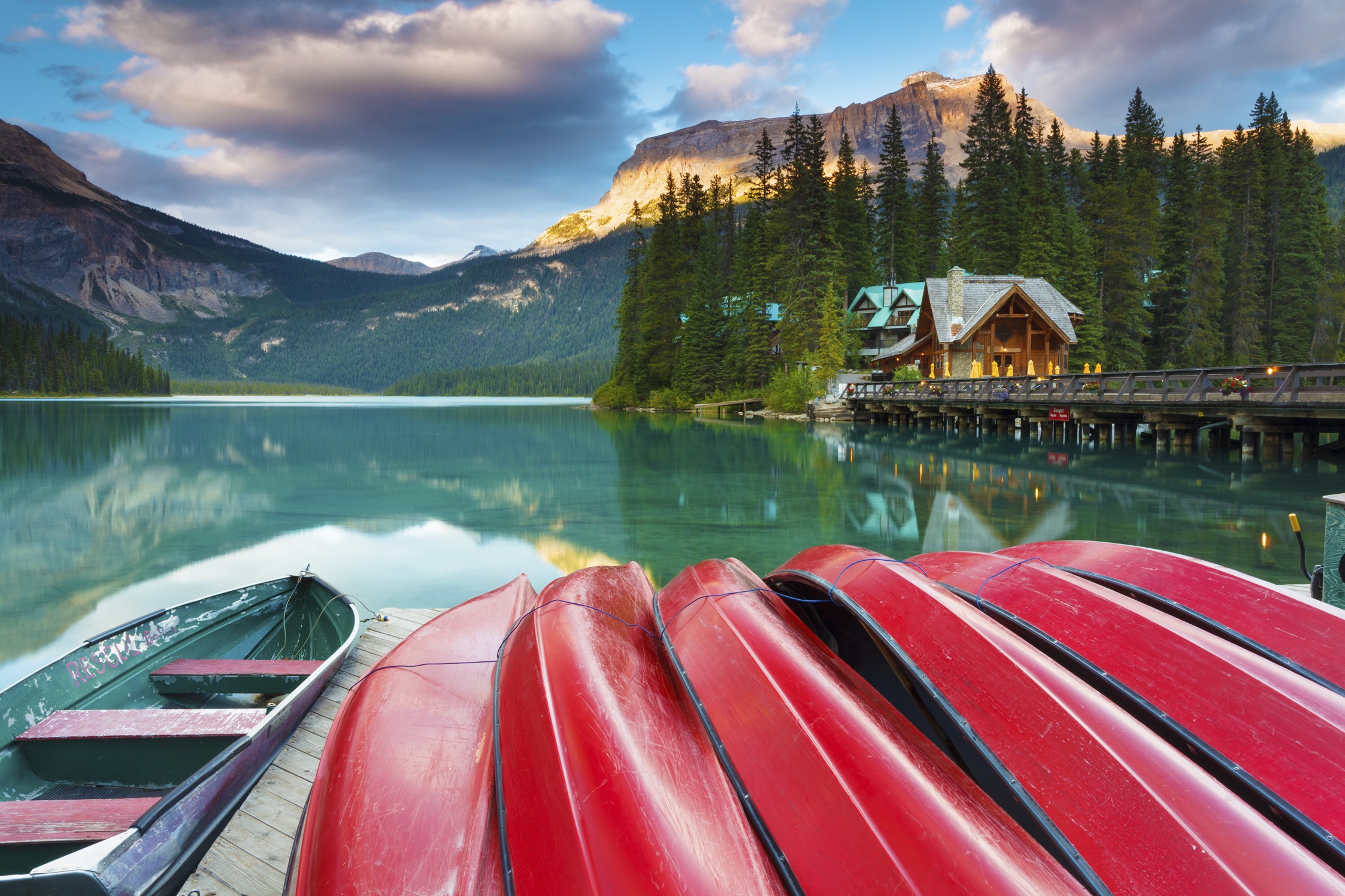 Bright red canoes rest on a wooden dock by a turquoise lake surrounded by pine forests and mountains, with a cosy lodge nearby — perfect for peaceful family getaways in the Canadian Rockies.