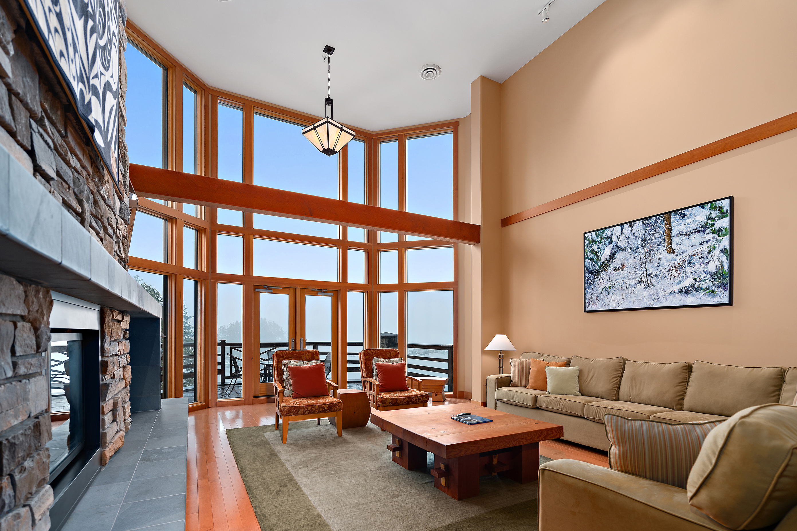 A high ceiling room in the Gillard Lodge featuring comfy furniture, a stone fireplace and large windows