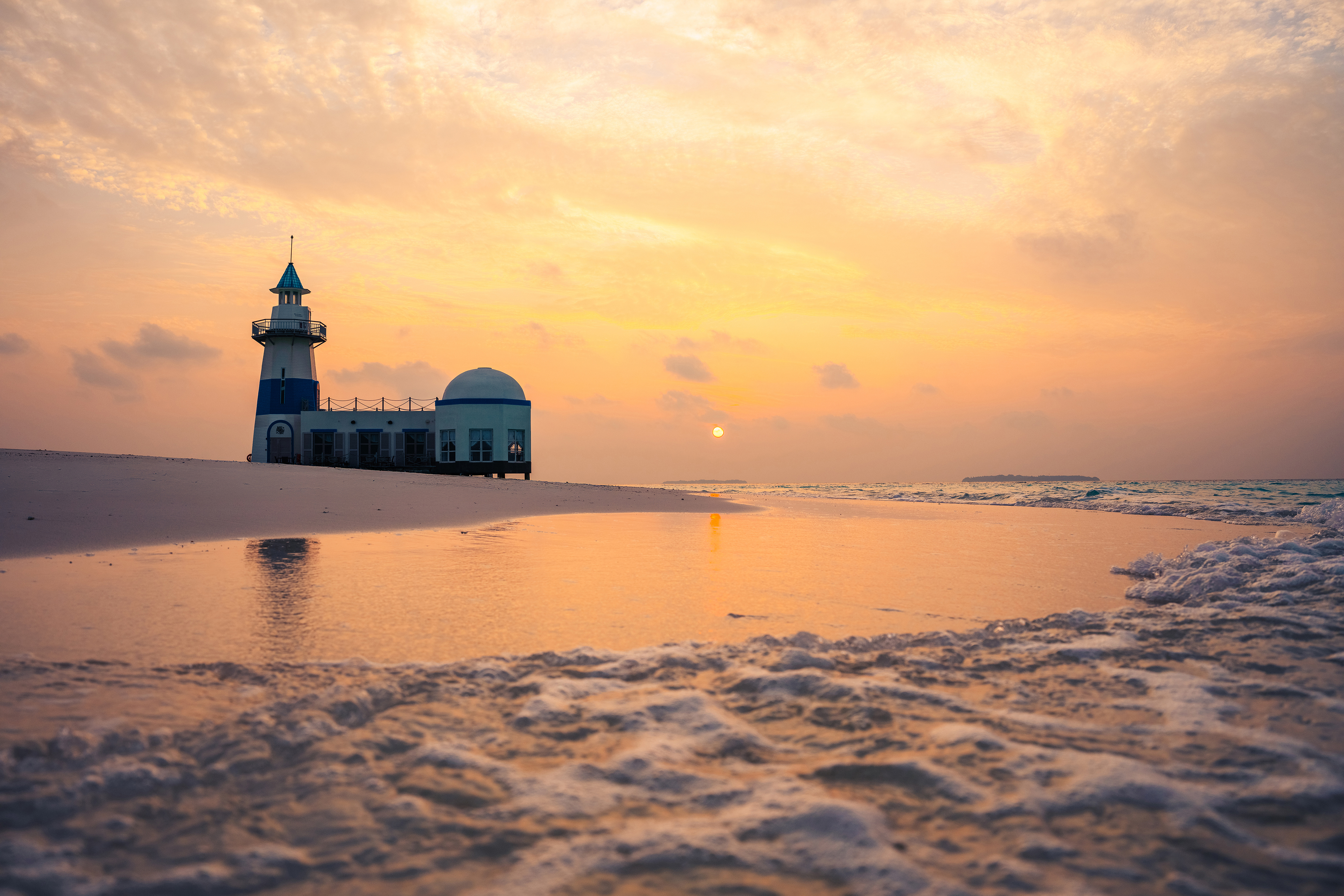 Sunset view of The Lighthouse Restaurant on the beach at InterContinental Maldives with gentle waves in the foreground.