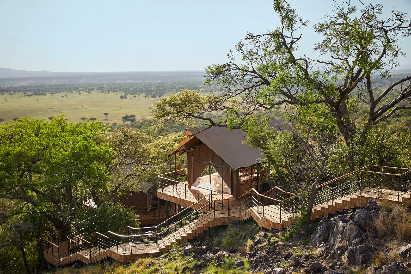 Luxury safari tent on a hillside, connected by wooden walkways and surrounded by trees with sweeping savannah views.
