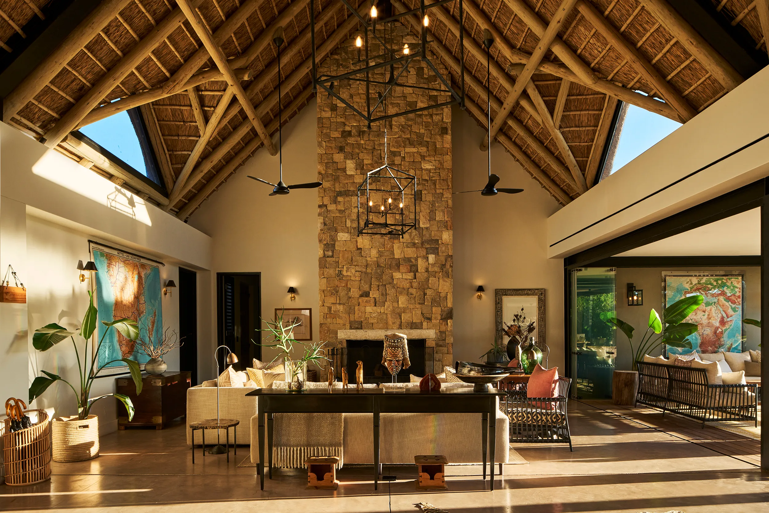The airy living room of the villa at Monwana Game Reserve featuring large vaulted ceilings, a tall stone fireplace, a square lounge area and stylish decor with maps hanging on the walls