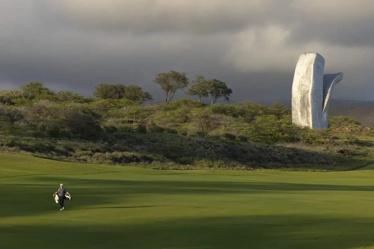 A person walking across the golf course at Four Seasons Lanai with a large sculpture in the background 
