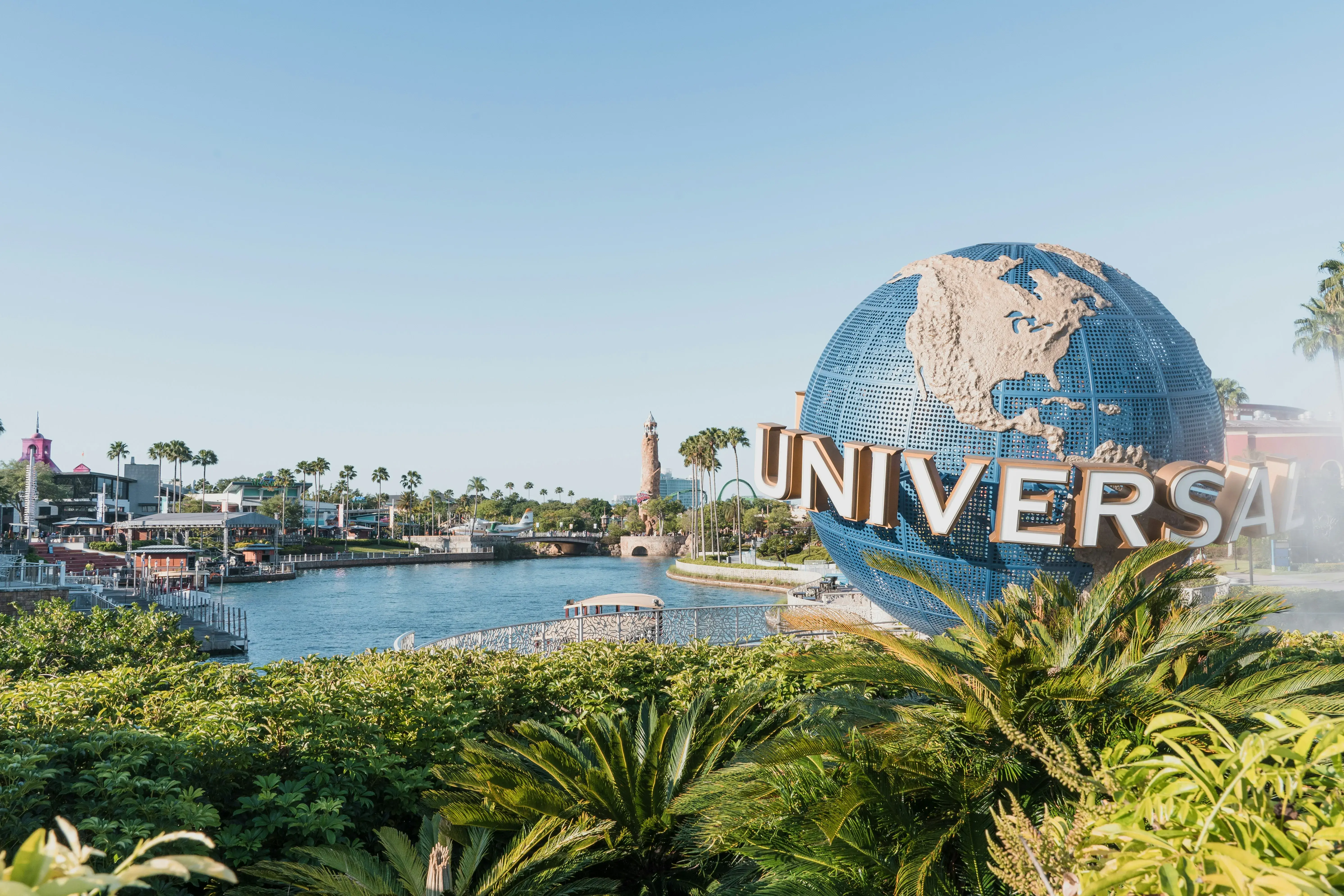 Universal Studios globe landmark overlooking a sunny waterfront with palm trees and park attractions.
