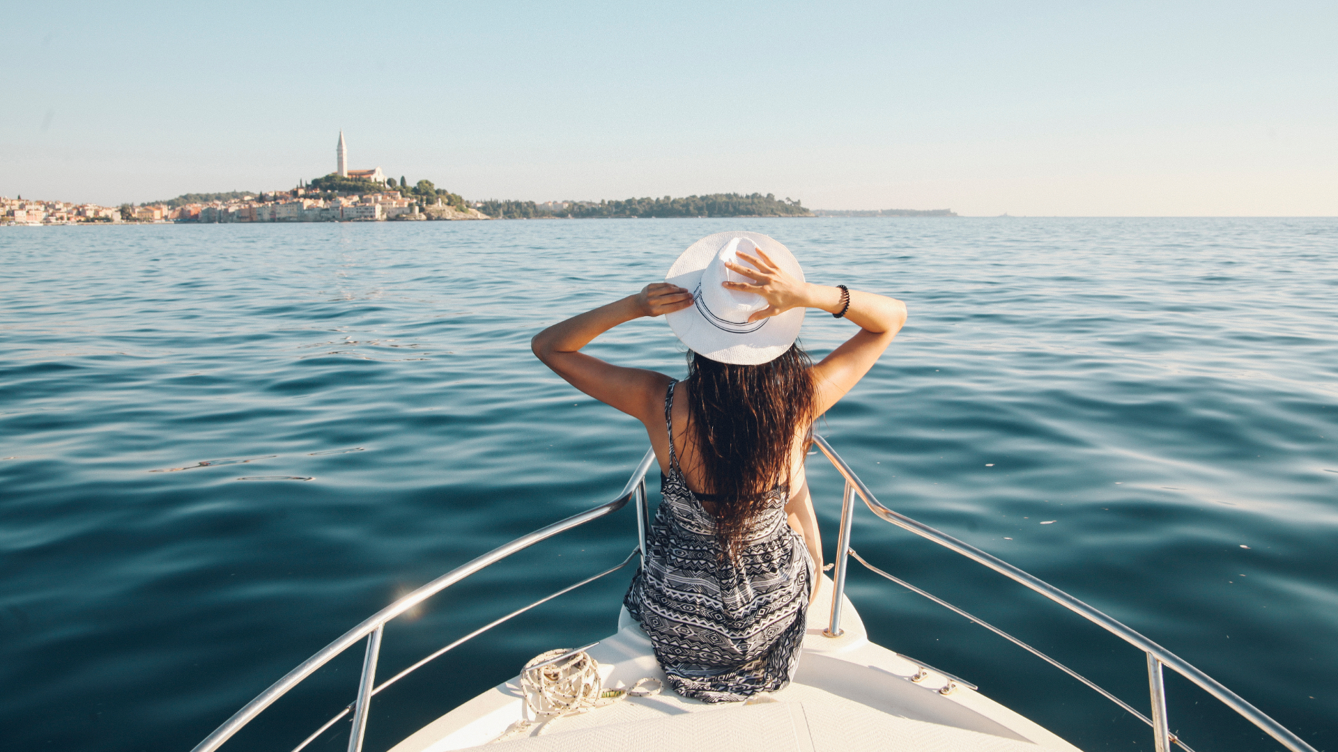 Woman sat at the front of a boat in the Adriatic sea. The town of Rovigno can be seen on the horizon