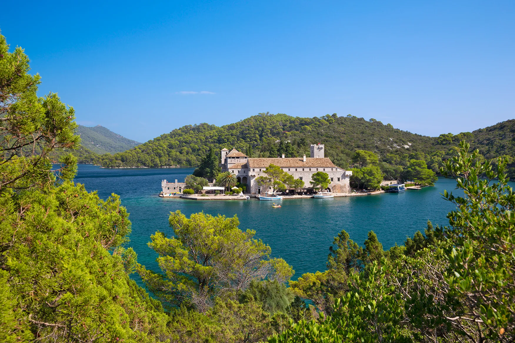 Historic monastery on a forested island surrounded by clear blue water.