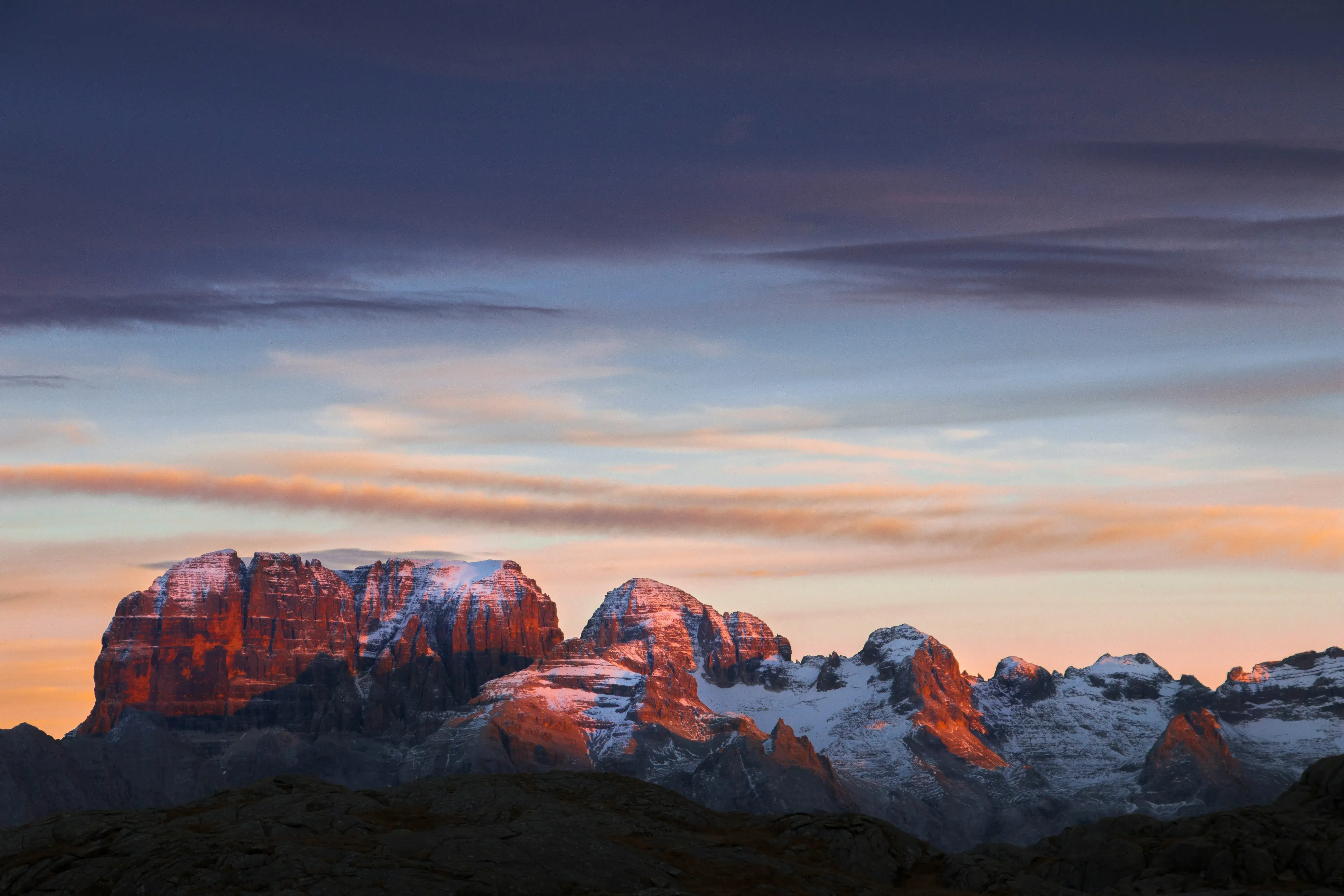 Snow-capped mountain peaks glowing with warm sunset light under a dramatic sky in the Dolomites.