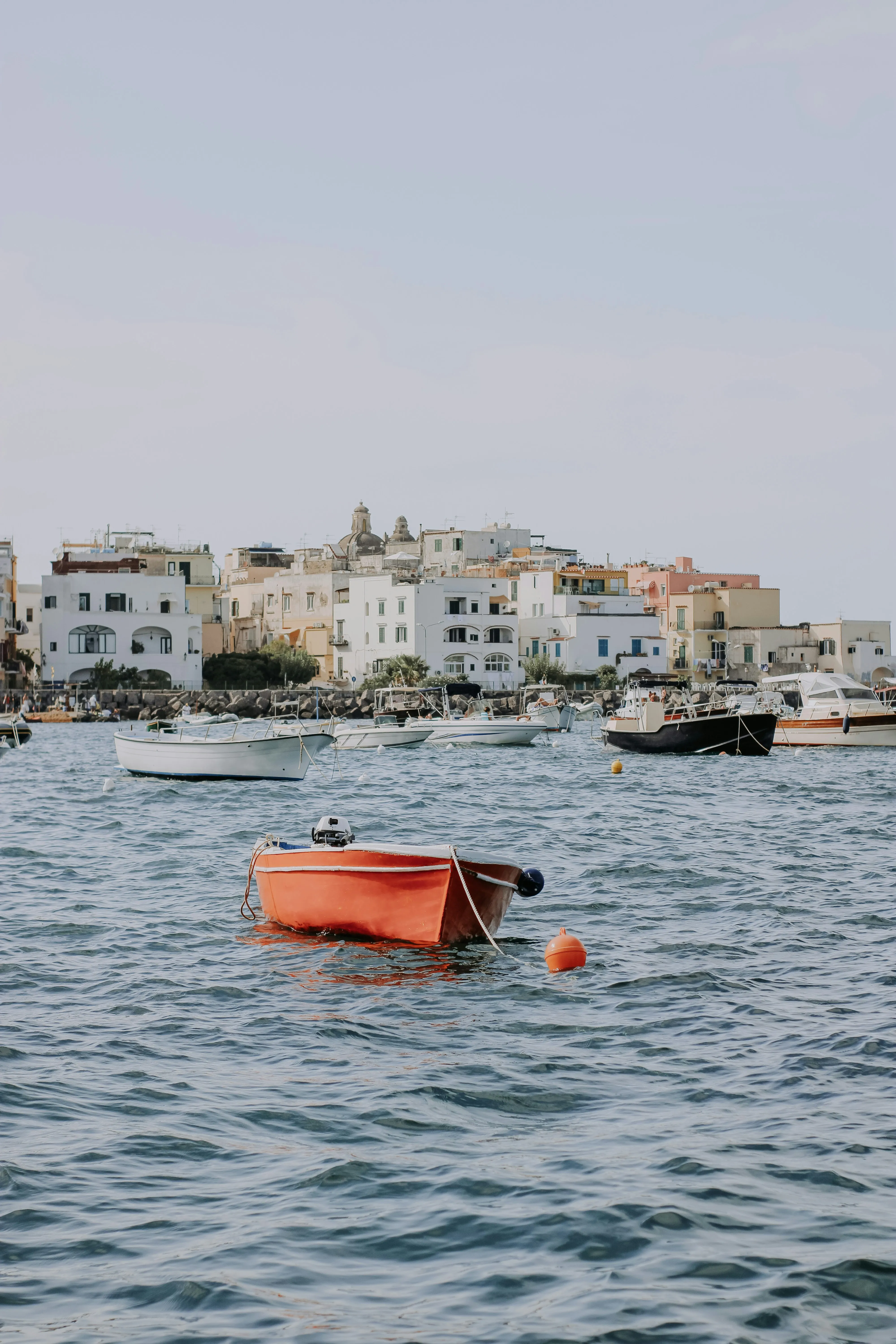 Small fishing boats floating on calm blue waters near the colorful coastal town of Ischia, Italy.