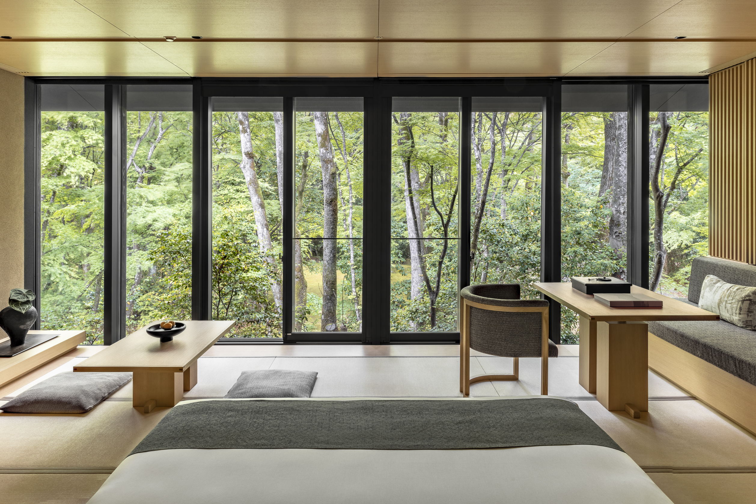 The Kaede Room at Aman Kyoto featuring stylish wooden furniture and a bed facing a large window that looks out over trees