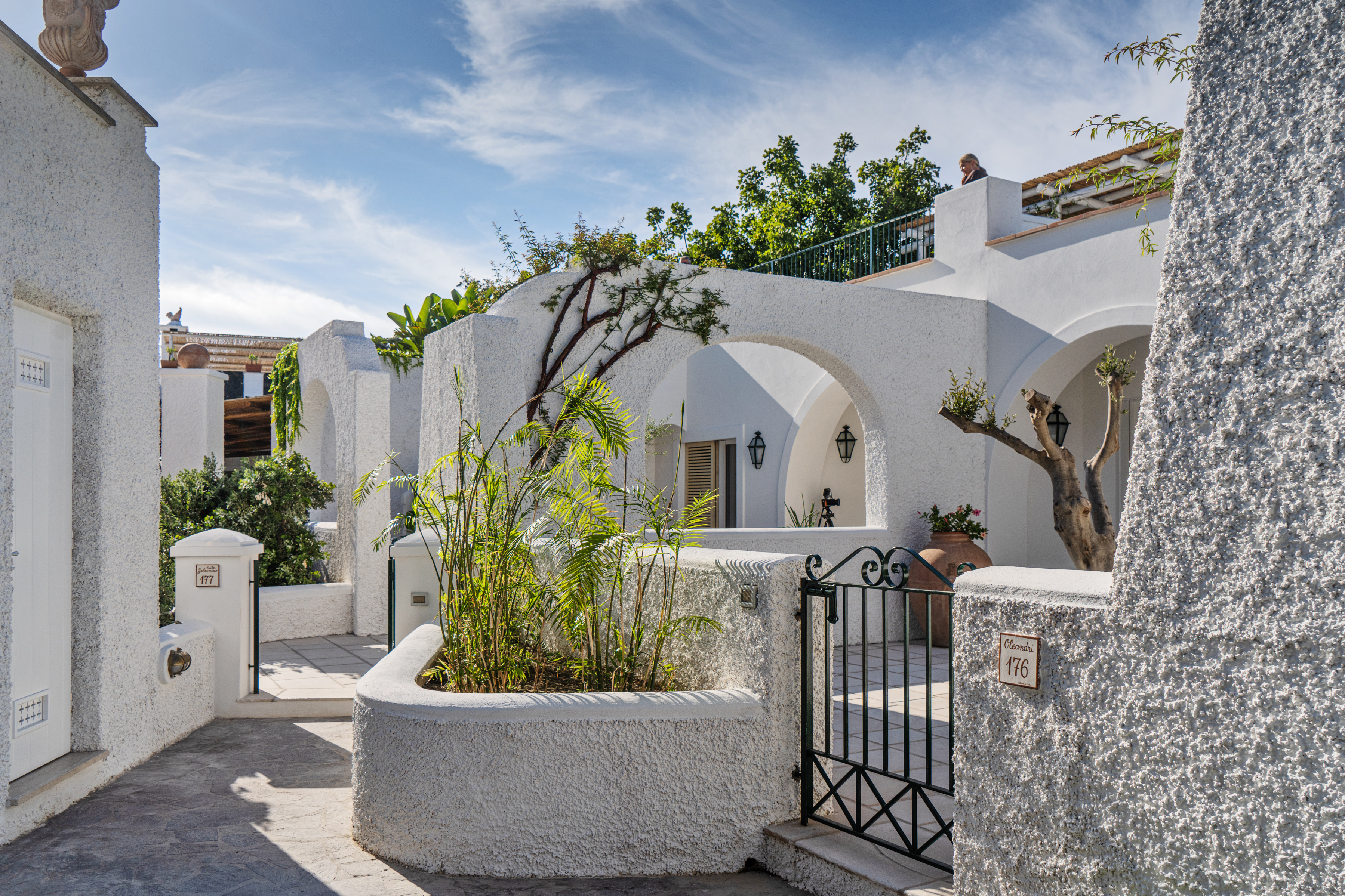 Beautiful courtyard at Botania Relais & Spa in Ischia with white stucco walls, lush greenery, and arched doorways under a clear blue sky.