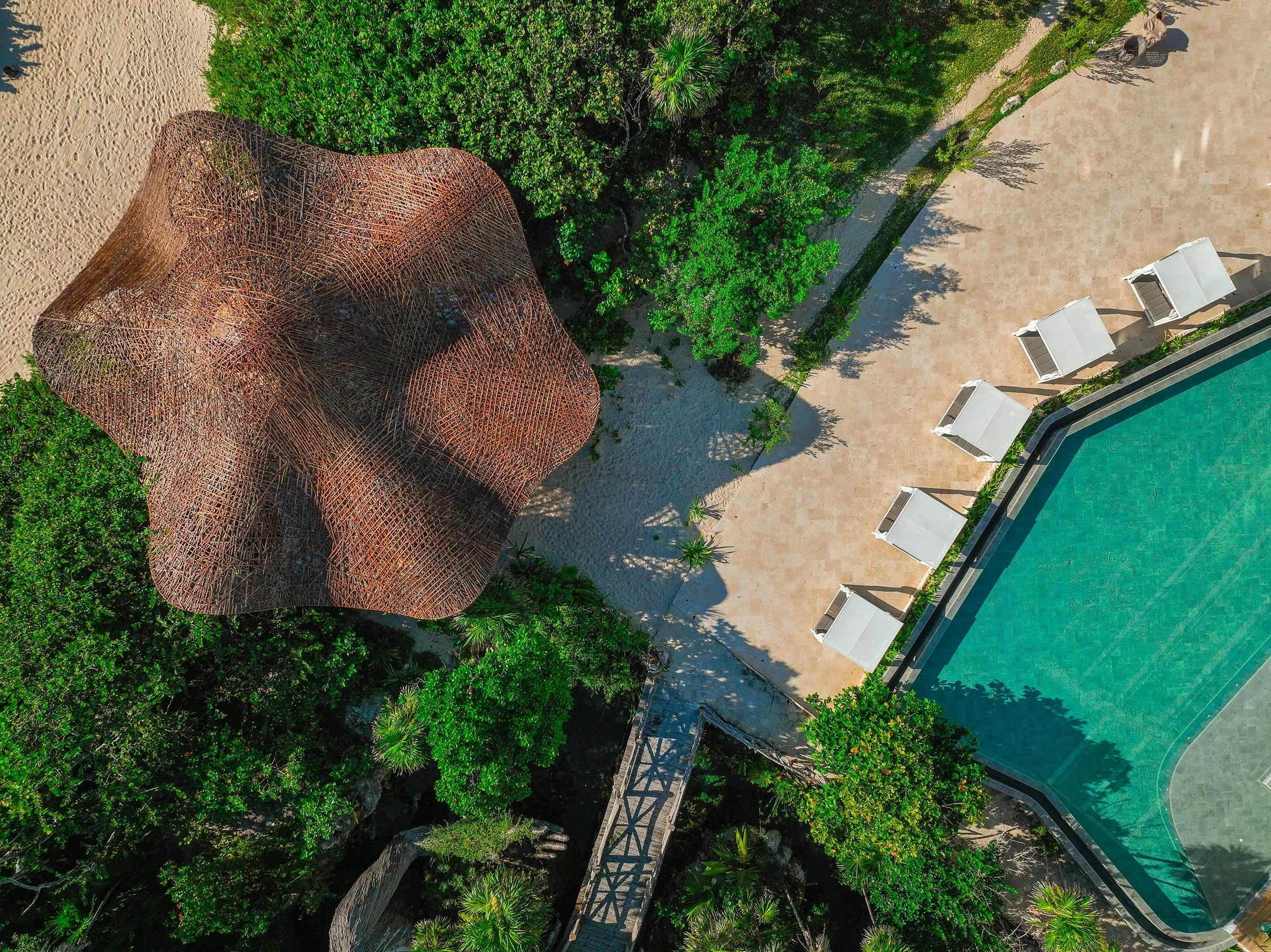 Aerial view of organic woven pavilion beside a pool surrounded by lush tropical greenery.