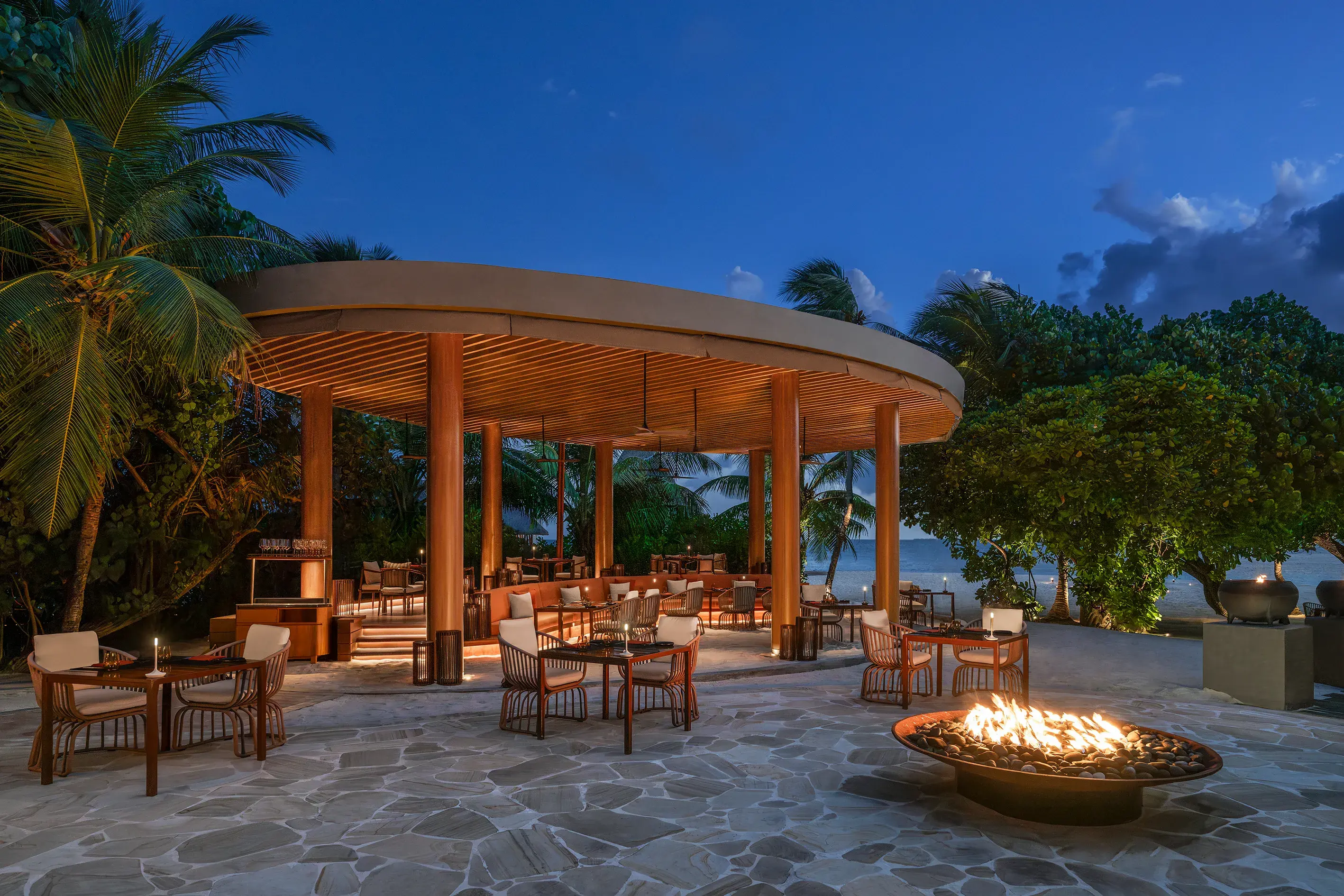 FIRE restaurant at W Maldives featuring elegant open-air beachfront dining, a glowing fire pit, tropical surroundings, and stunning Indian Ocean views under the evening sky