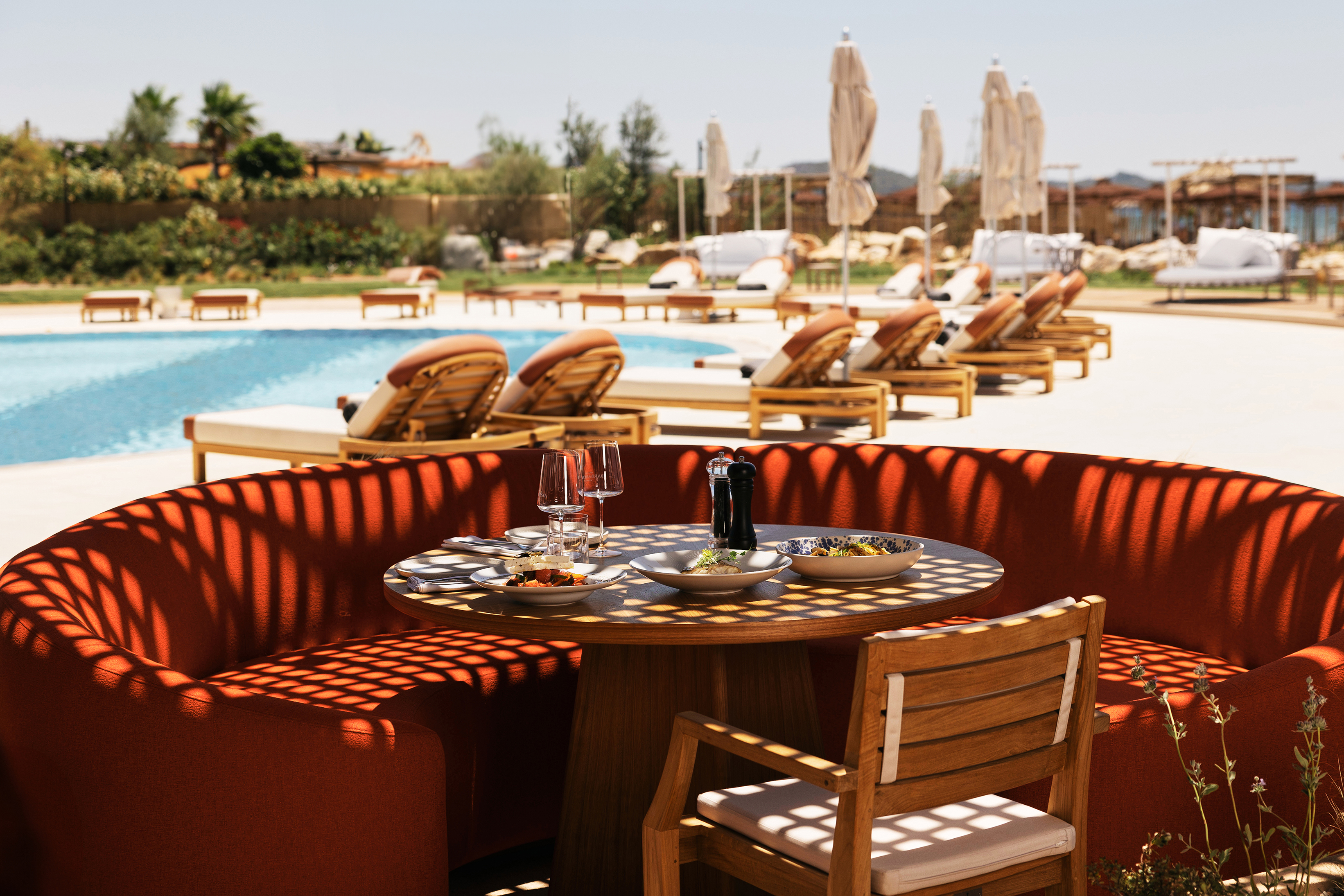 Red circular restaurant booth set up for a lunch for two beside a pool with loungers