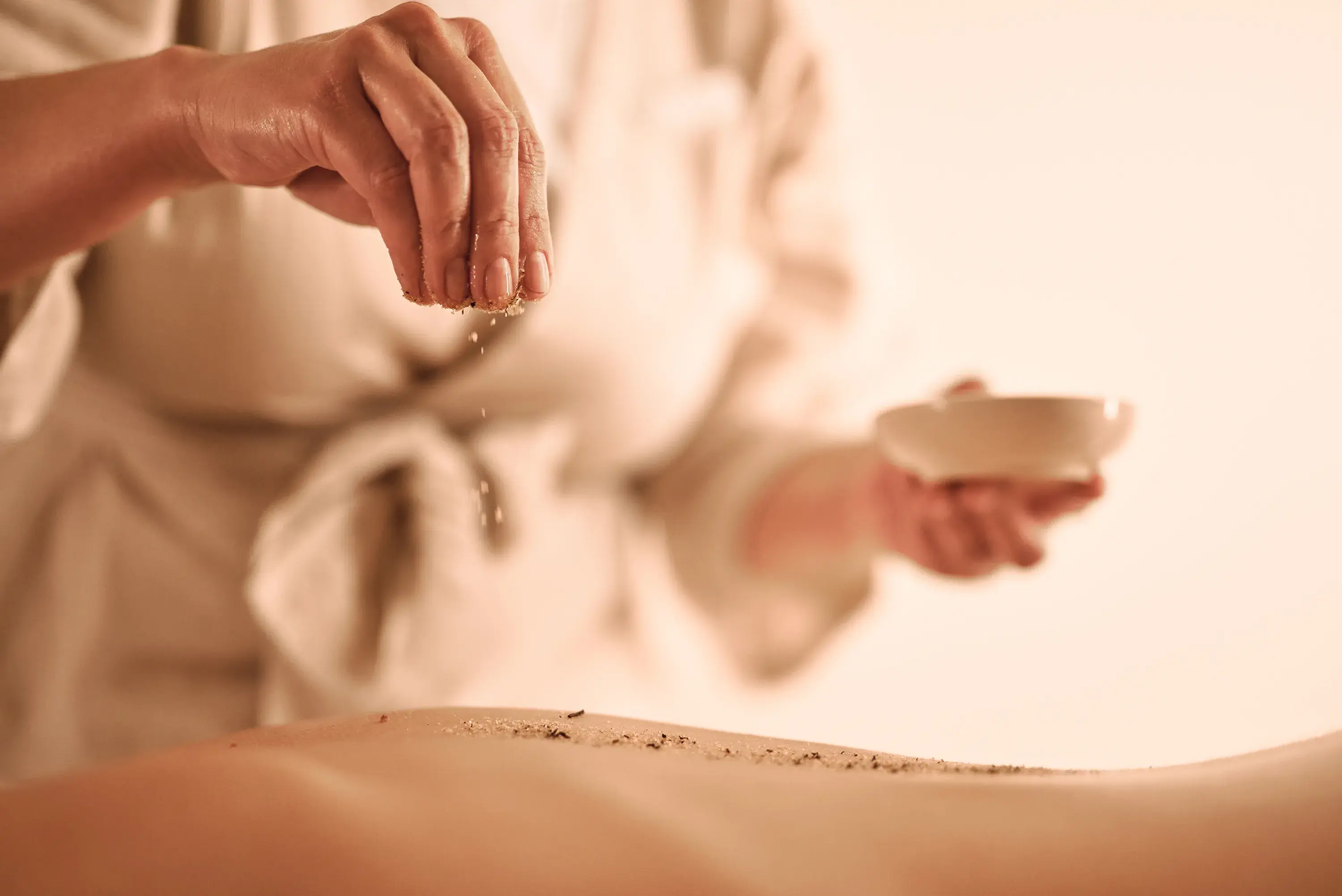 Close up of a spa therapist's hand sprinkling herbs on the back of a guest at Villa Dubrovnik in Croatia