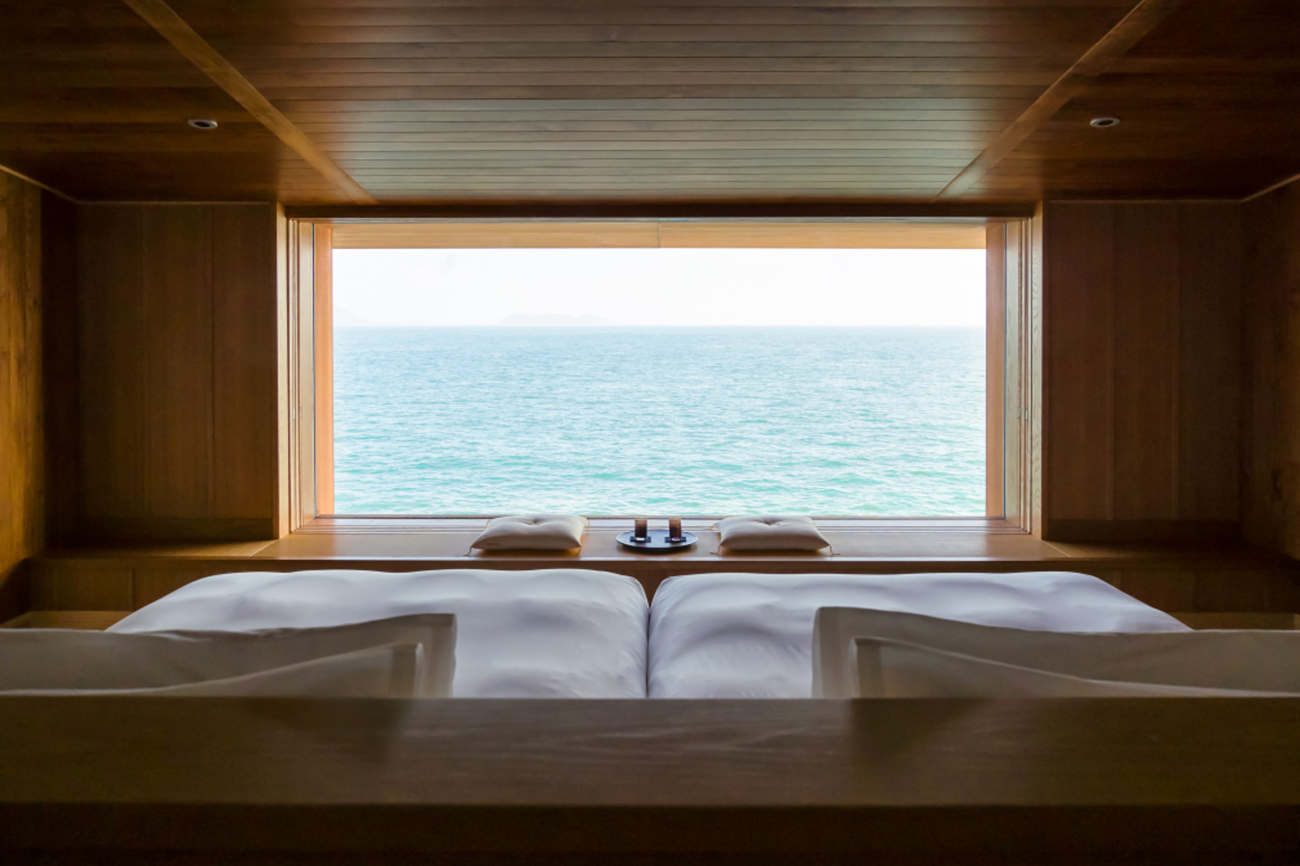 A view through a bedroom aboard Guntu featuring a large bed and traditional Japanese seating area facing a large window looking out to sea