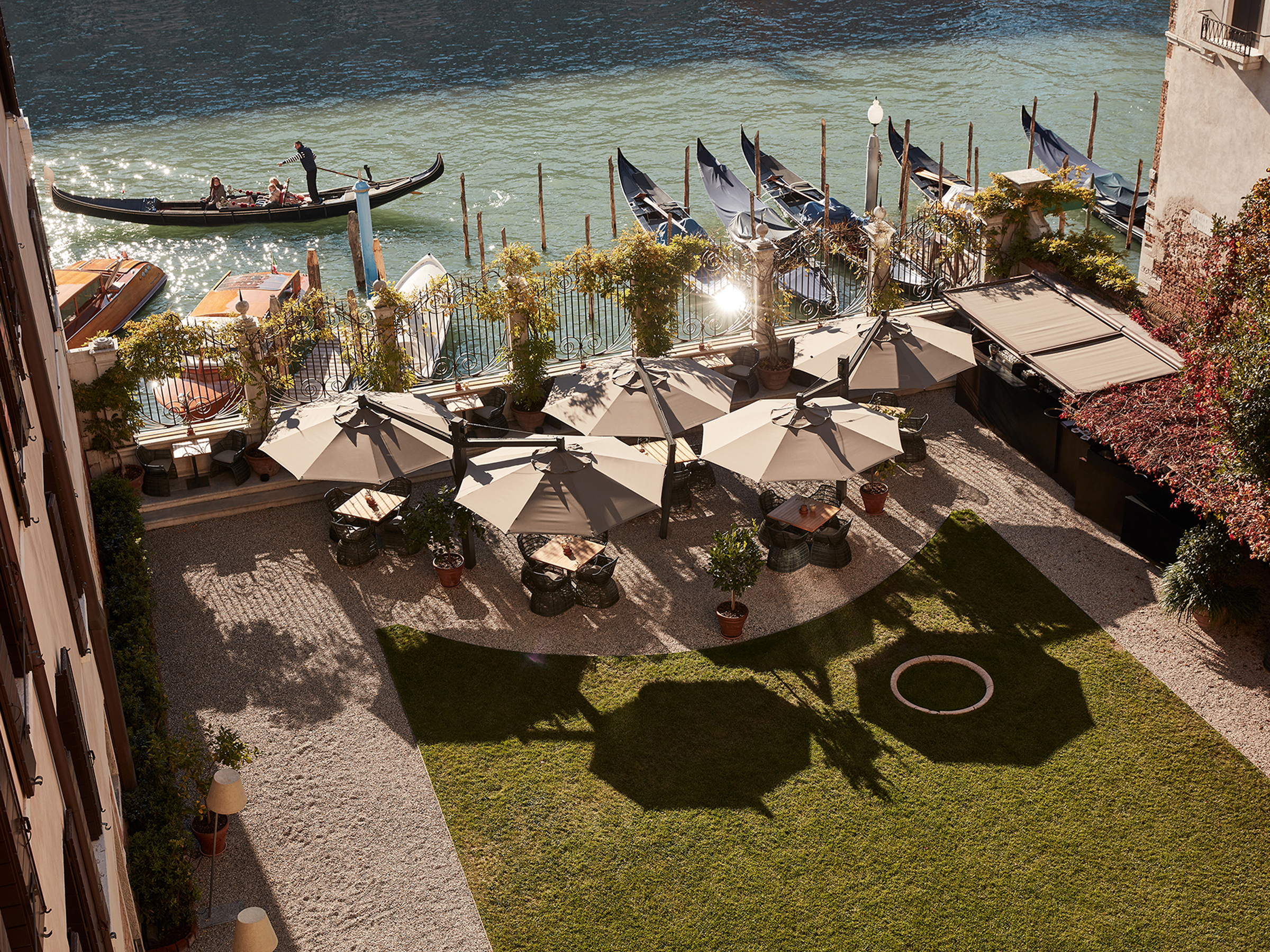 A waterside garden with tables under sun umbrellas and a gondola drifting by