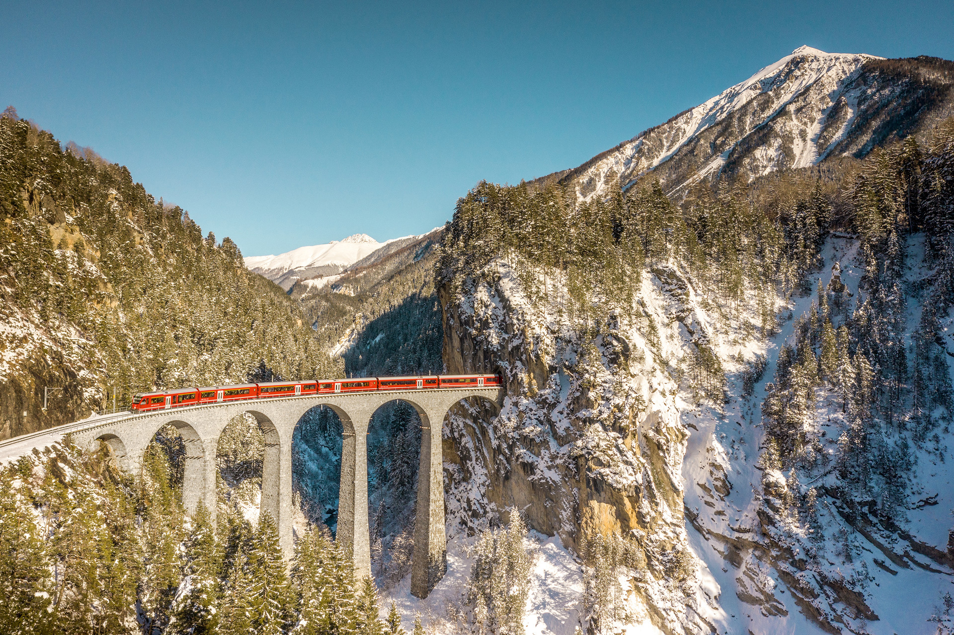 An aerial view of a train on a bridge as it passes over a valley
