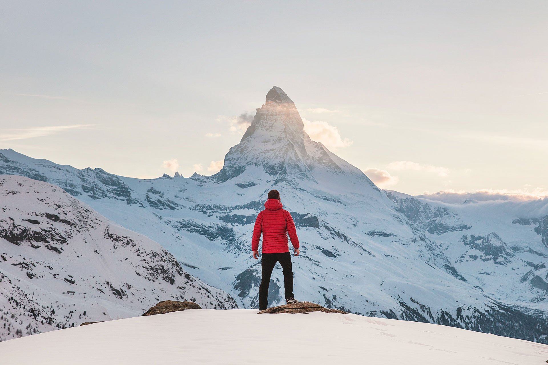 A man wearing a brown coat standing on a snowy hill looking towards the Matterhorn