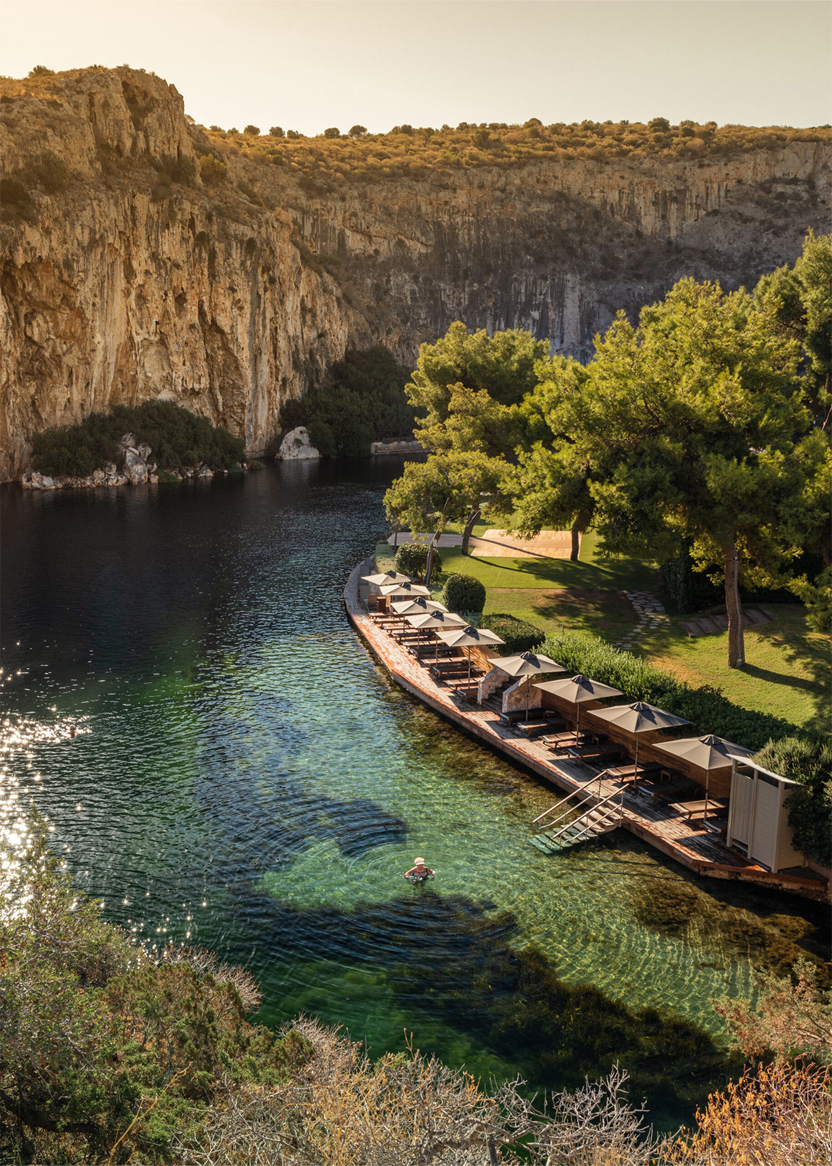 An aerial view of someone taking a dip in Lake Vougliameni surrounded by rocky cliffs