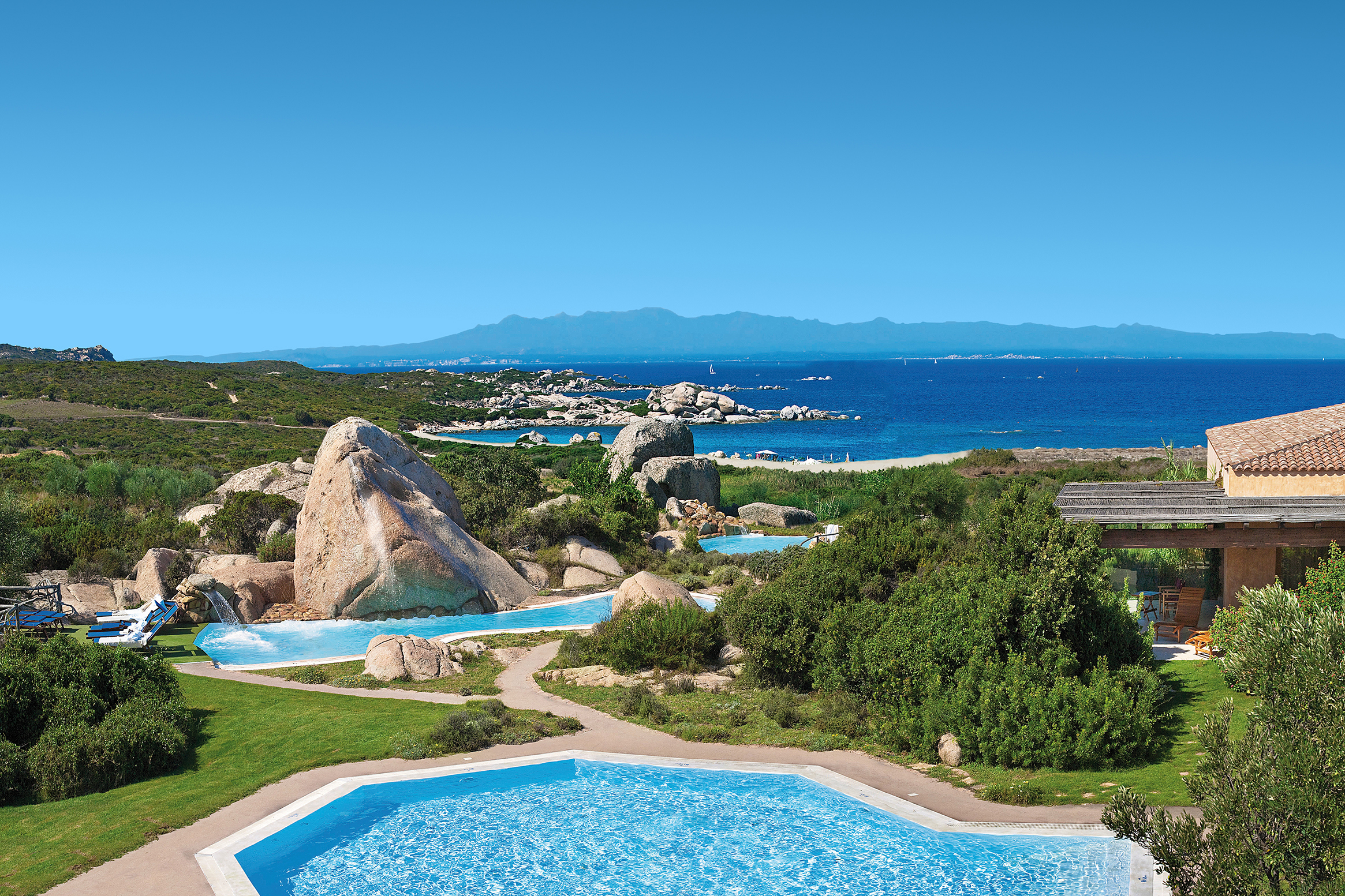 A view of tiered pools heading down through greenery and rocks towards the ocean