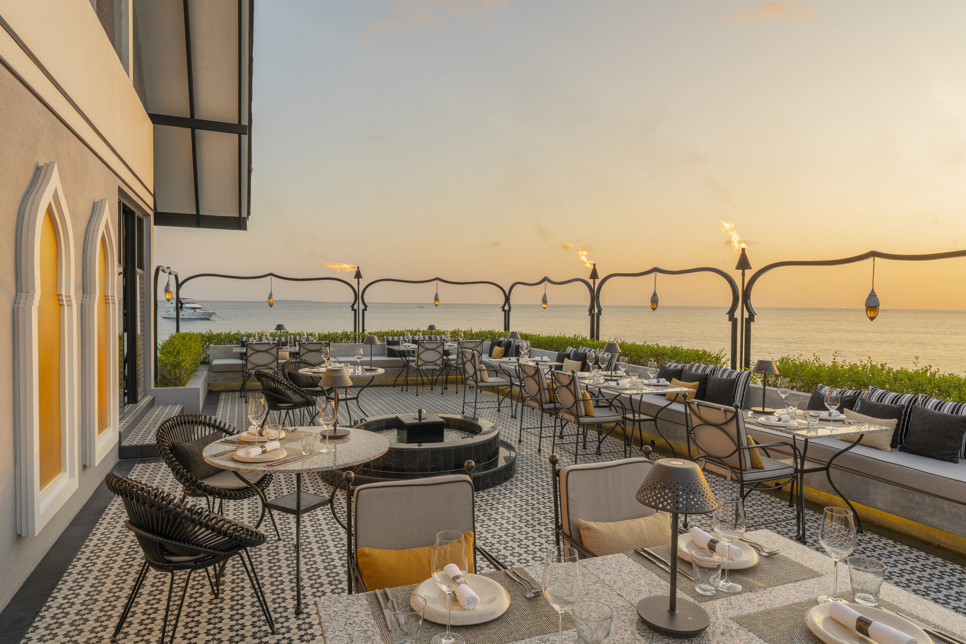 Ourdoor dining tables of a restaurant set up for dinner on a tiled terrace with flaming torches