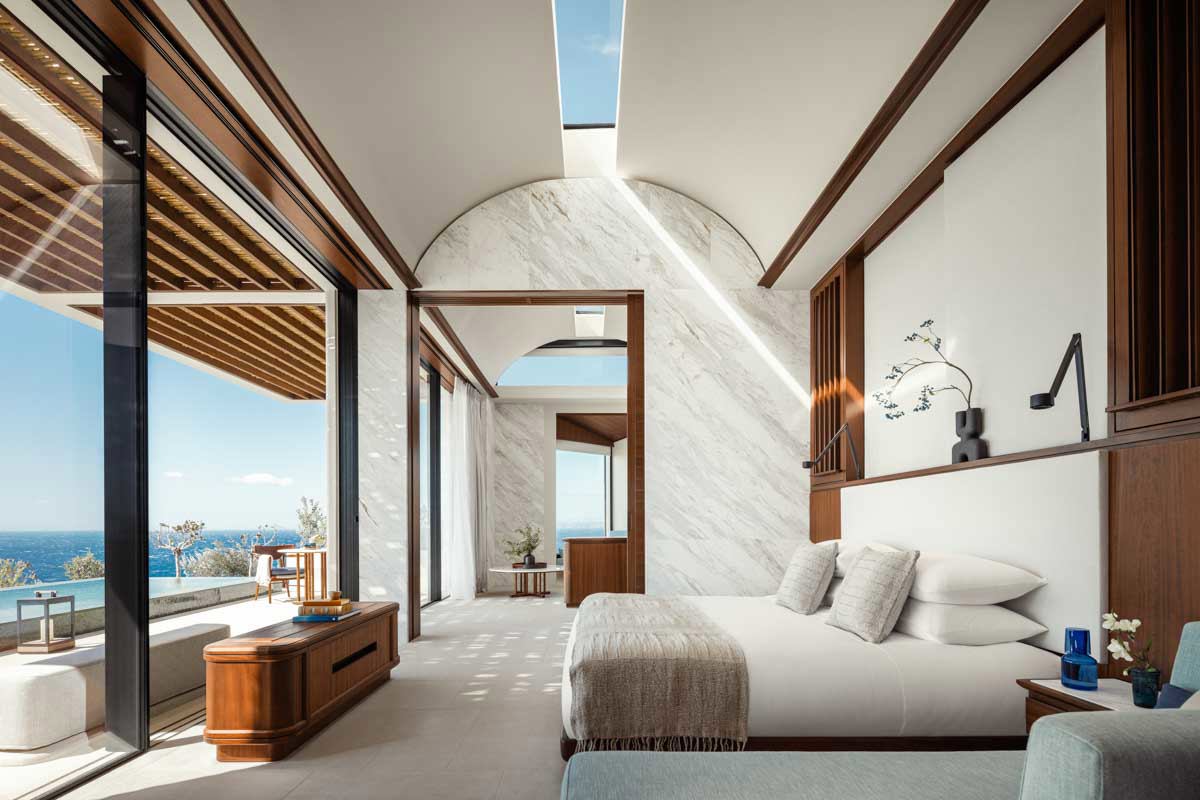 A serene bedroom in white, teak and marble with high domed ceilings and classic furniture at One&Only Kea Island