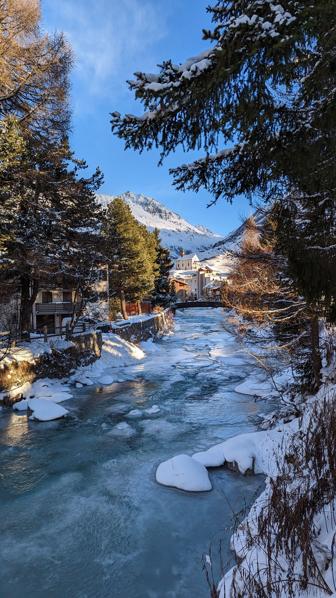 A frozen river between trees and buildings in Andermatt