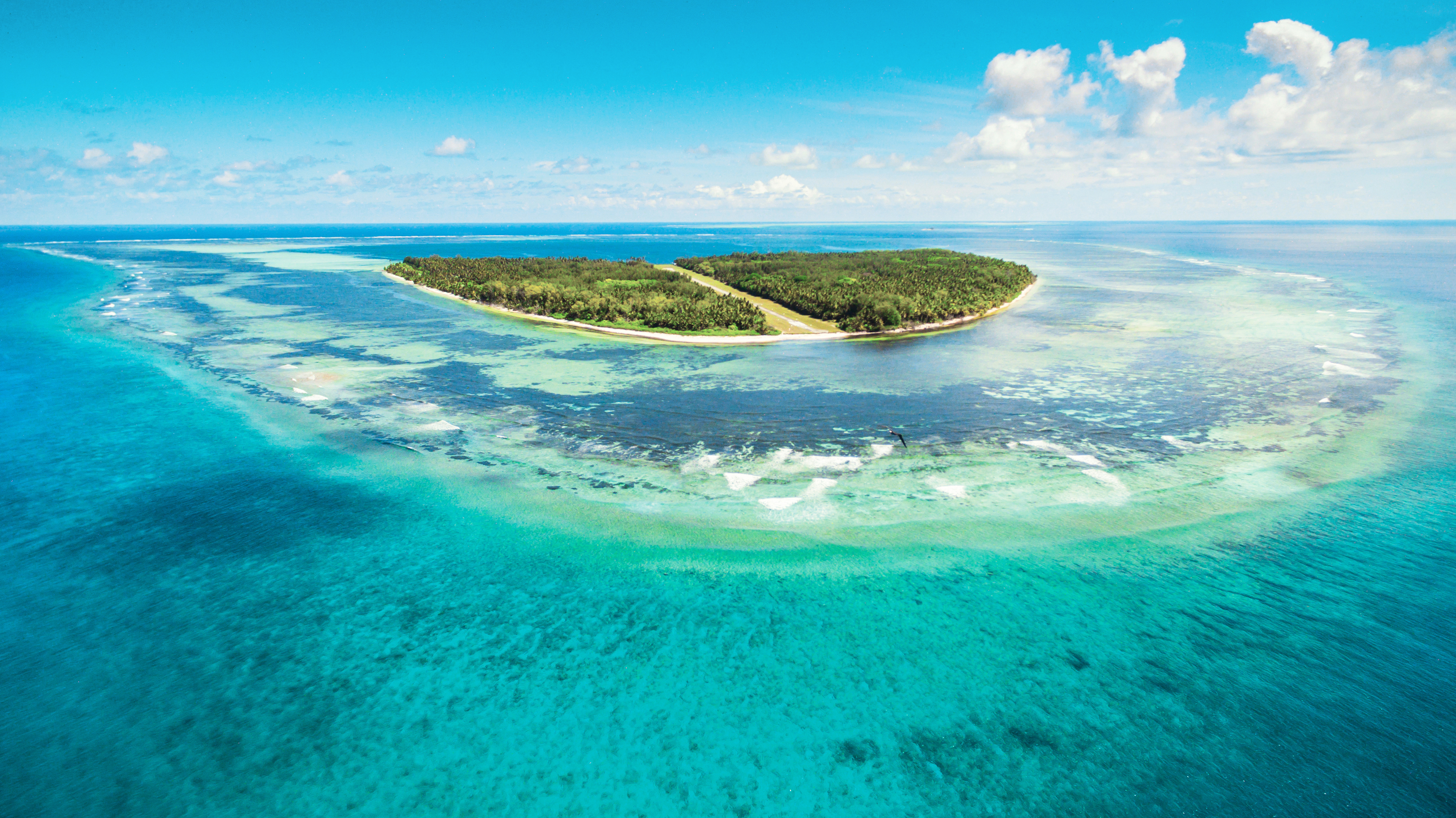 A vast pcean landscape with a lush green island surrounded  by reefs in the centre