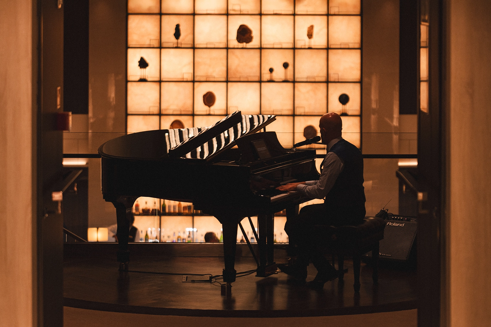 A man playing the piano in low lighting in the lobby of the Explora I cruise ship