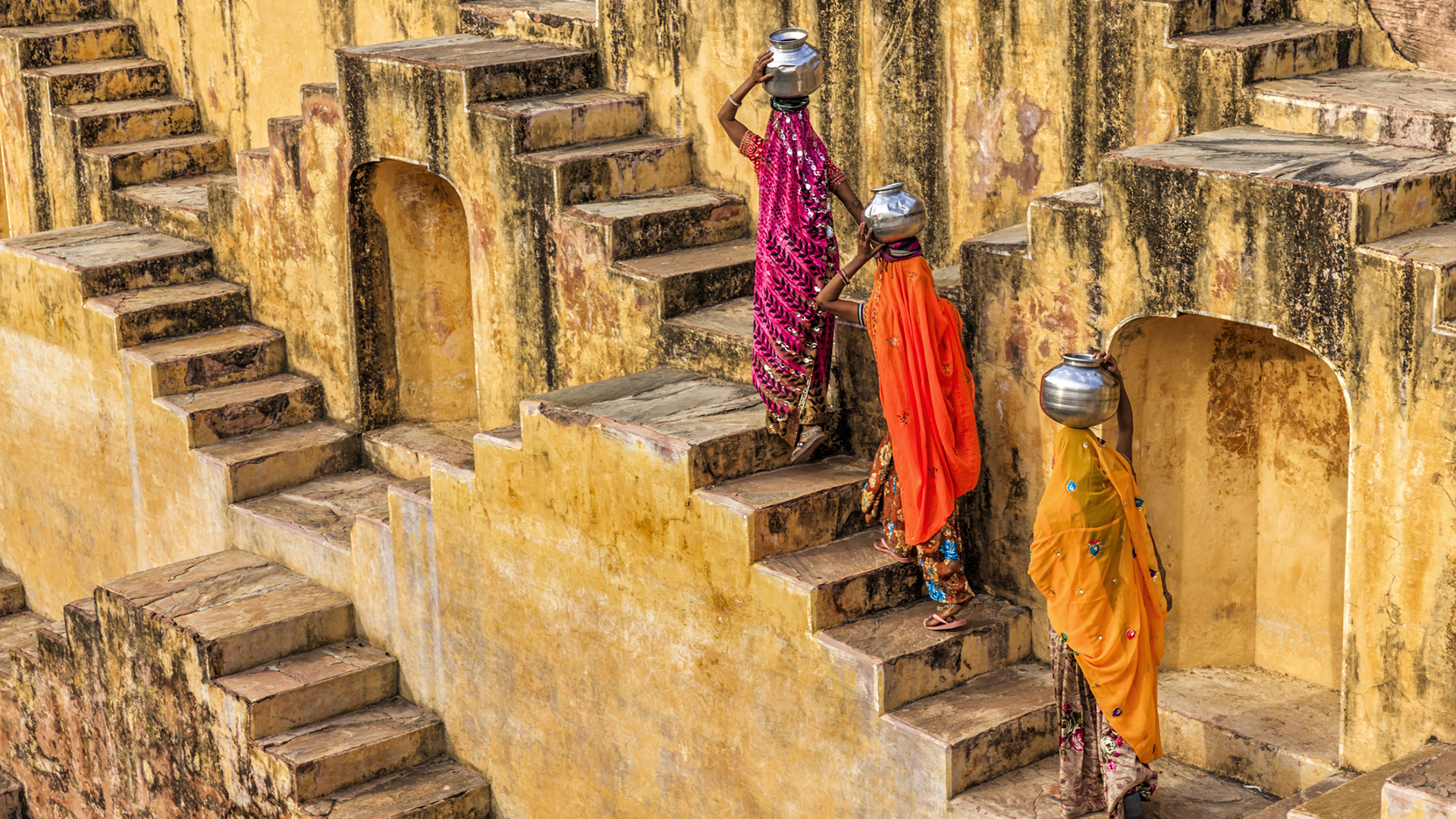 Three women in colourful sarees walking up a stepwell in Jaipur