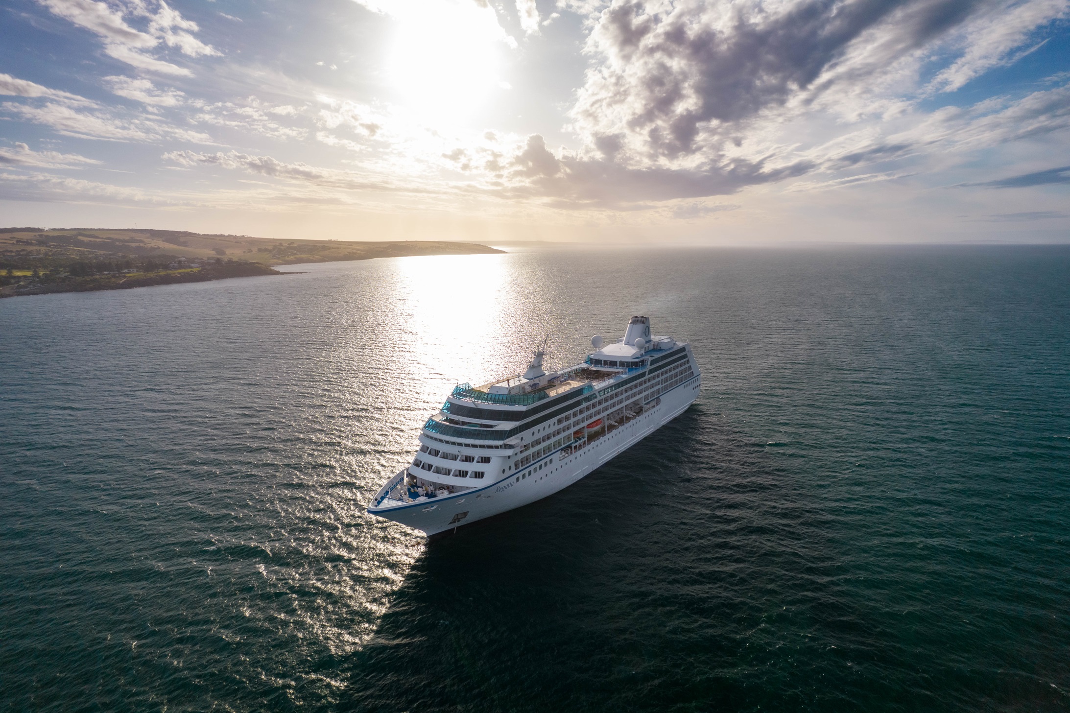 Oceania Cruises Regatta ship sailing on a calm ocean under a partly cloudy sky with bright sunlight.